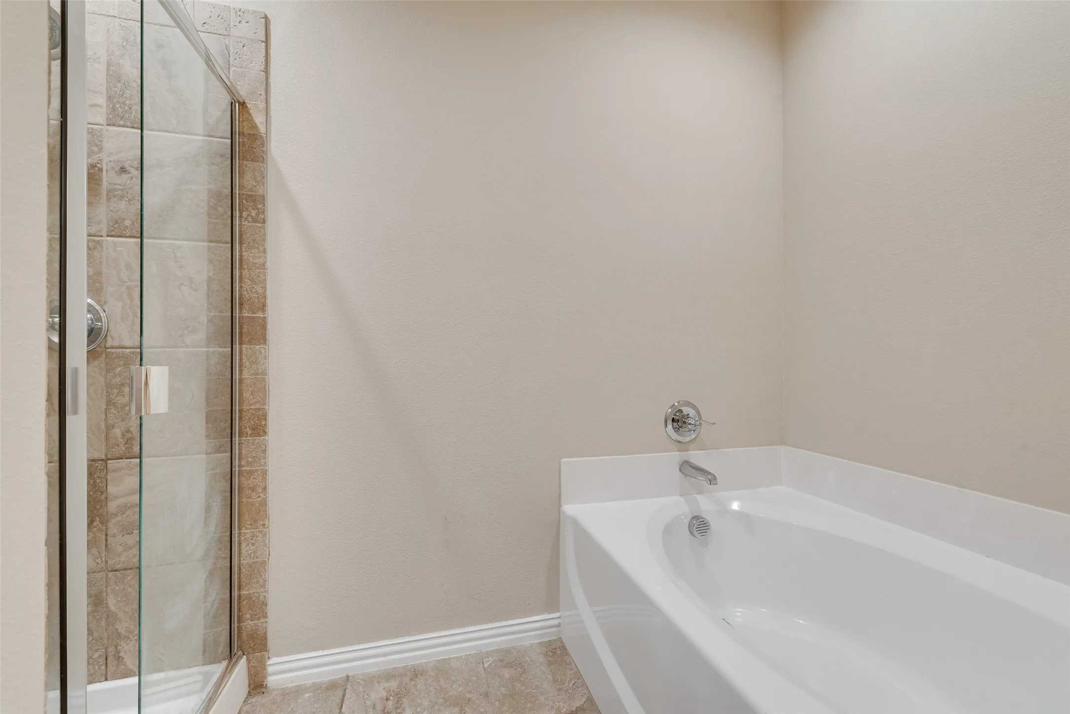 Bathtub with chrome fixtures, tiled shower surround, and glass shower enclosure