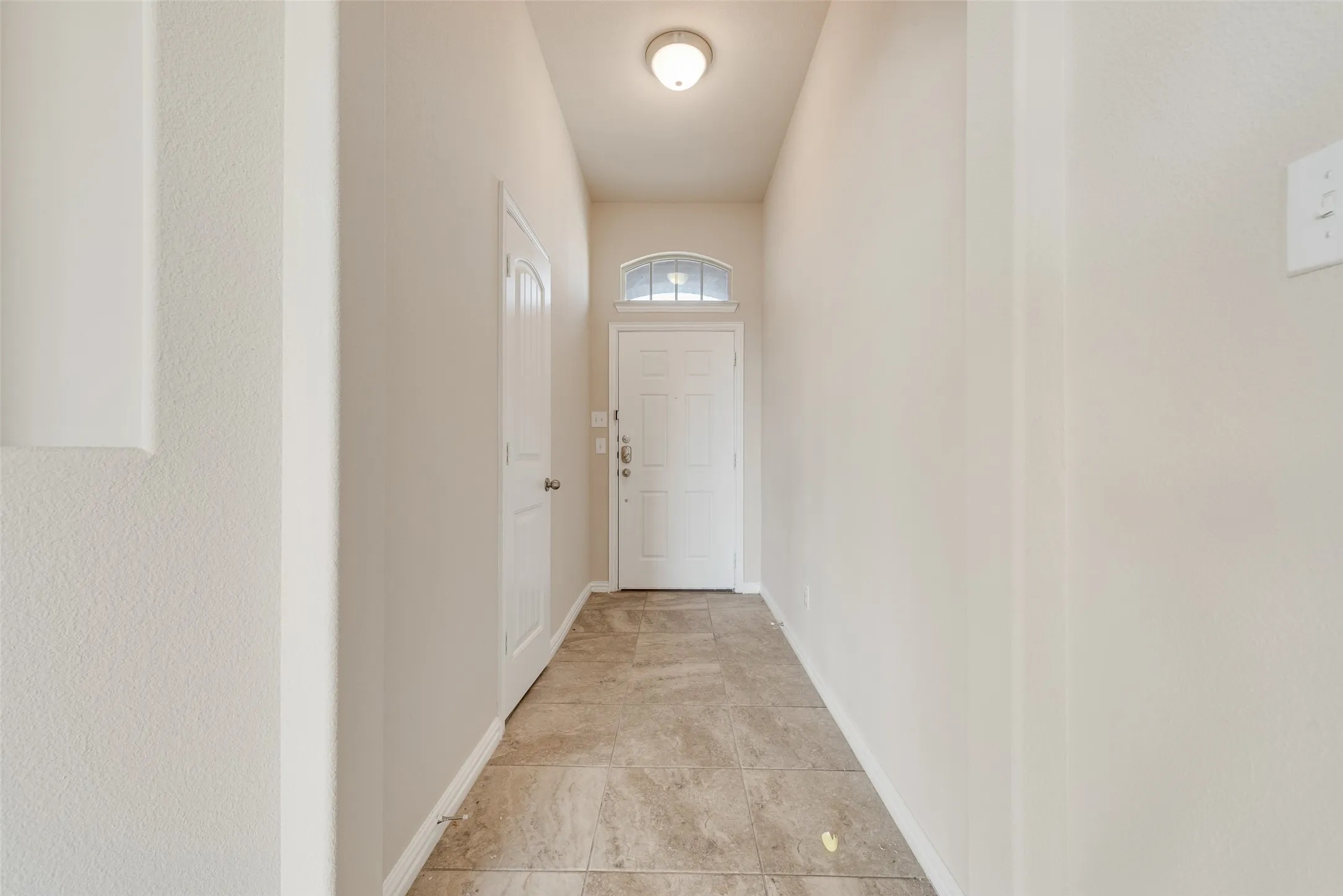 Foyer featuring ceramic tile flooring, a white paneled door with an arched transom, and a flush-mount ceiling light fixture