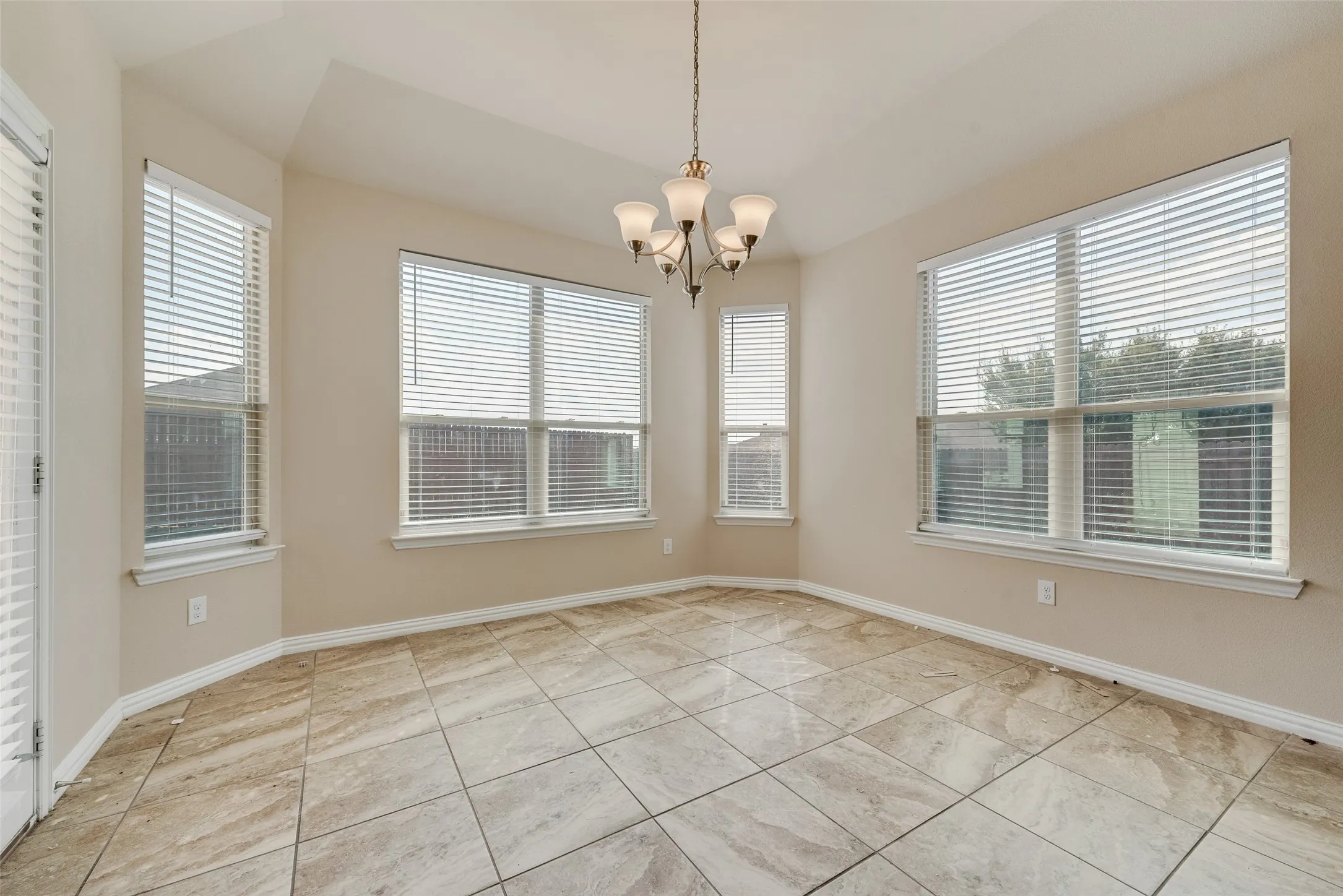 Recessed ceiling with a chandelier, bay windows with blinds, and square tile flooring