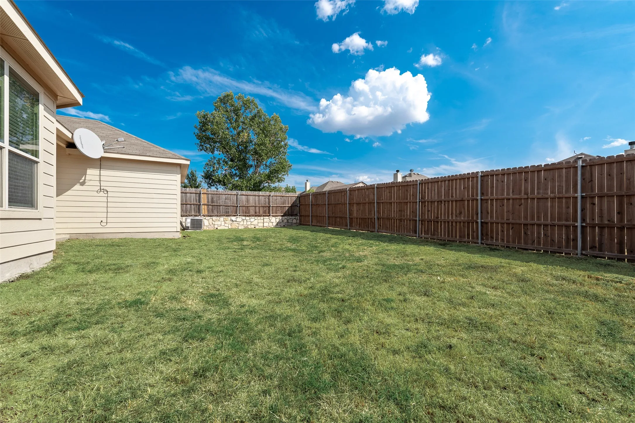 Expansive grassy yard with a privacy fence and stone retaining wall