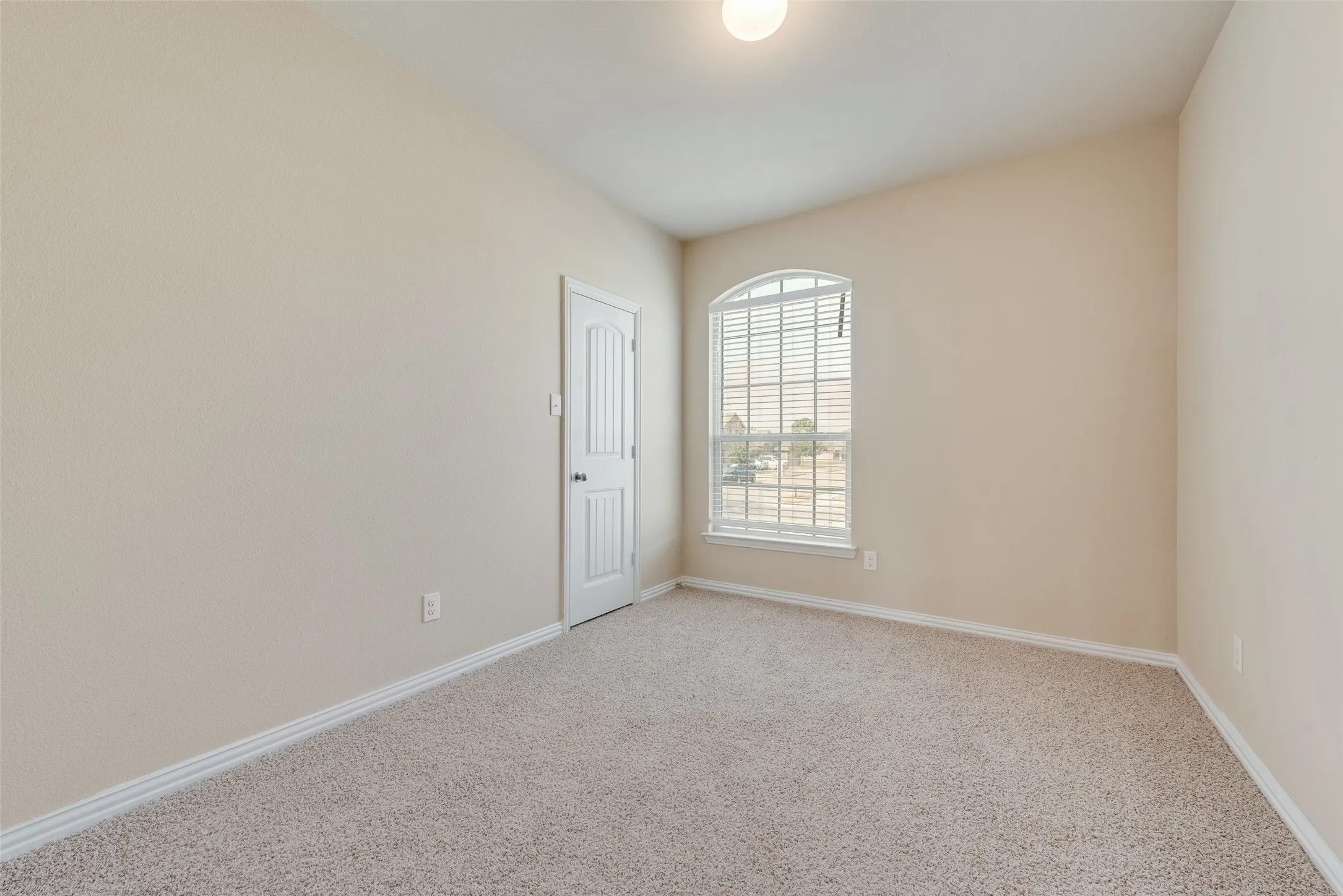 Arched window with blinds, vaulted ceiling, and neutral carpet flooring