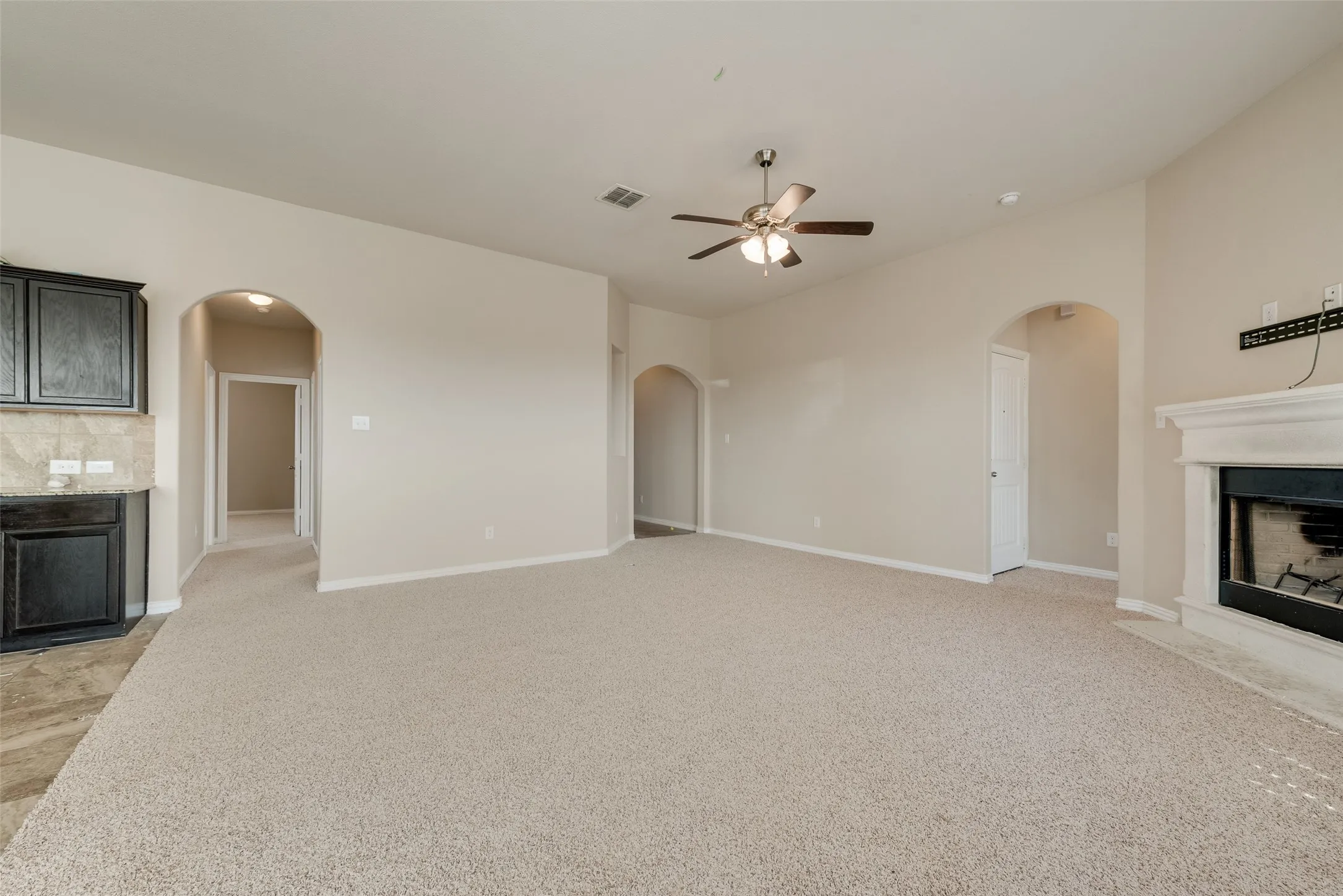Recessed fireplace with a white mantel, ceiling fan with light fixture, arched doorways, and light-toned carpeting
