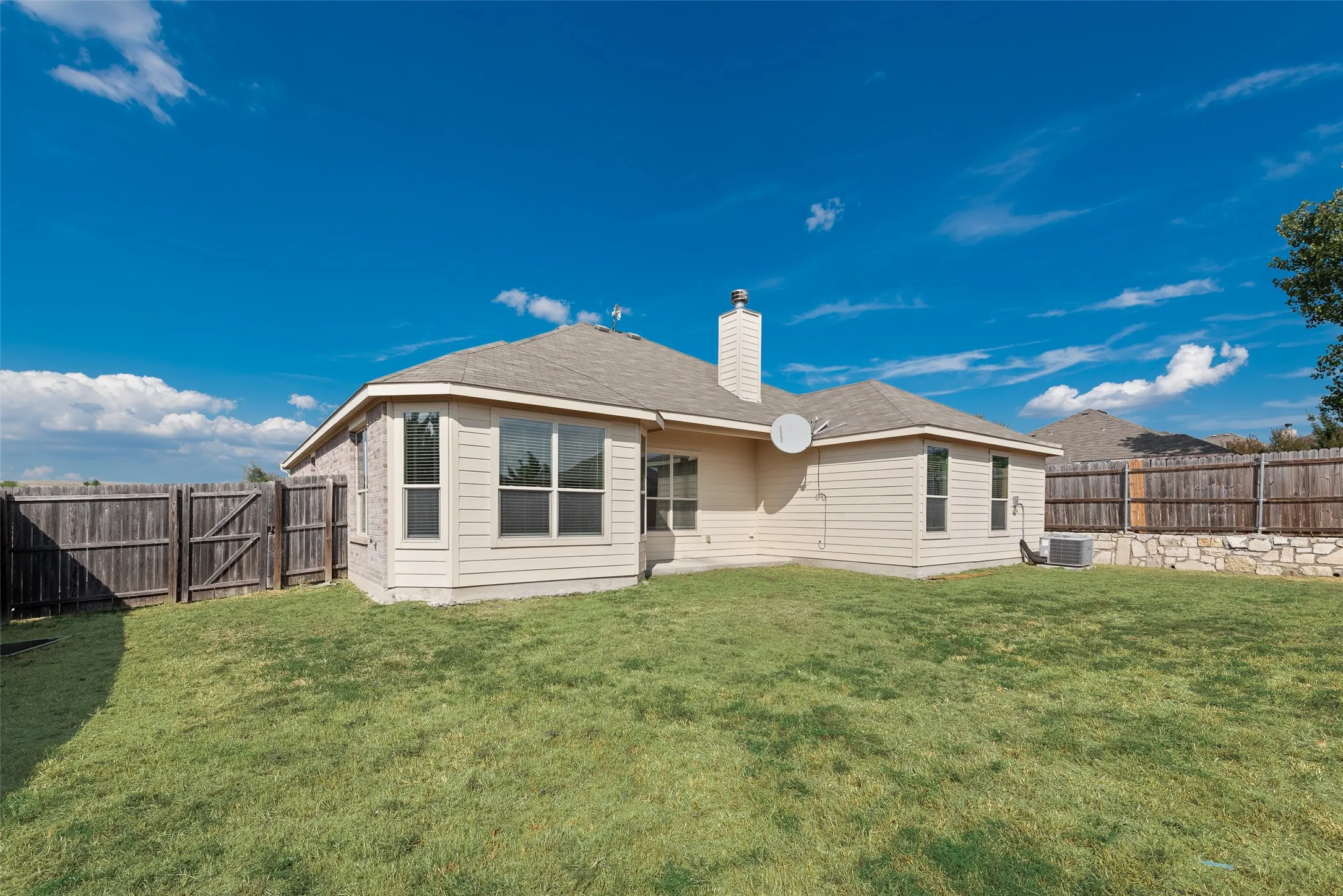 Expansive backyard featuring a wood privacy fence, stone retaining wall, and a multi-pane bay window