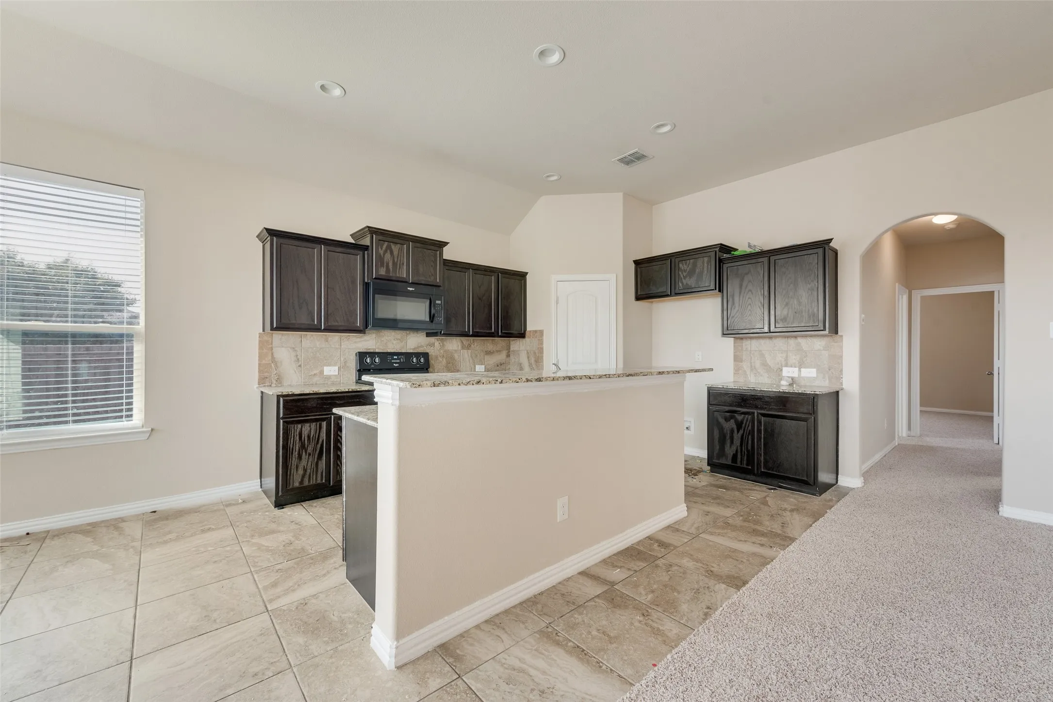 Kitchen area featuring dark wood-finish cabinetry, light-toned tiled flooring, recessed lighting, and a breakfast bar