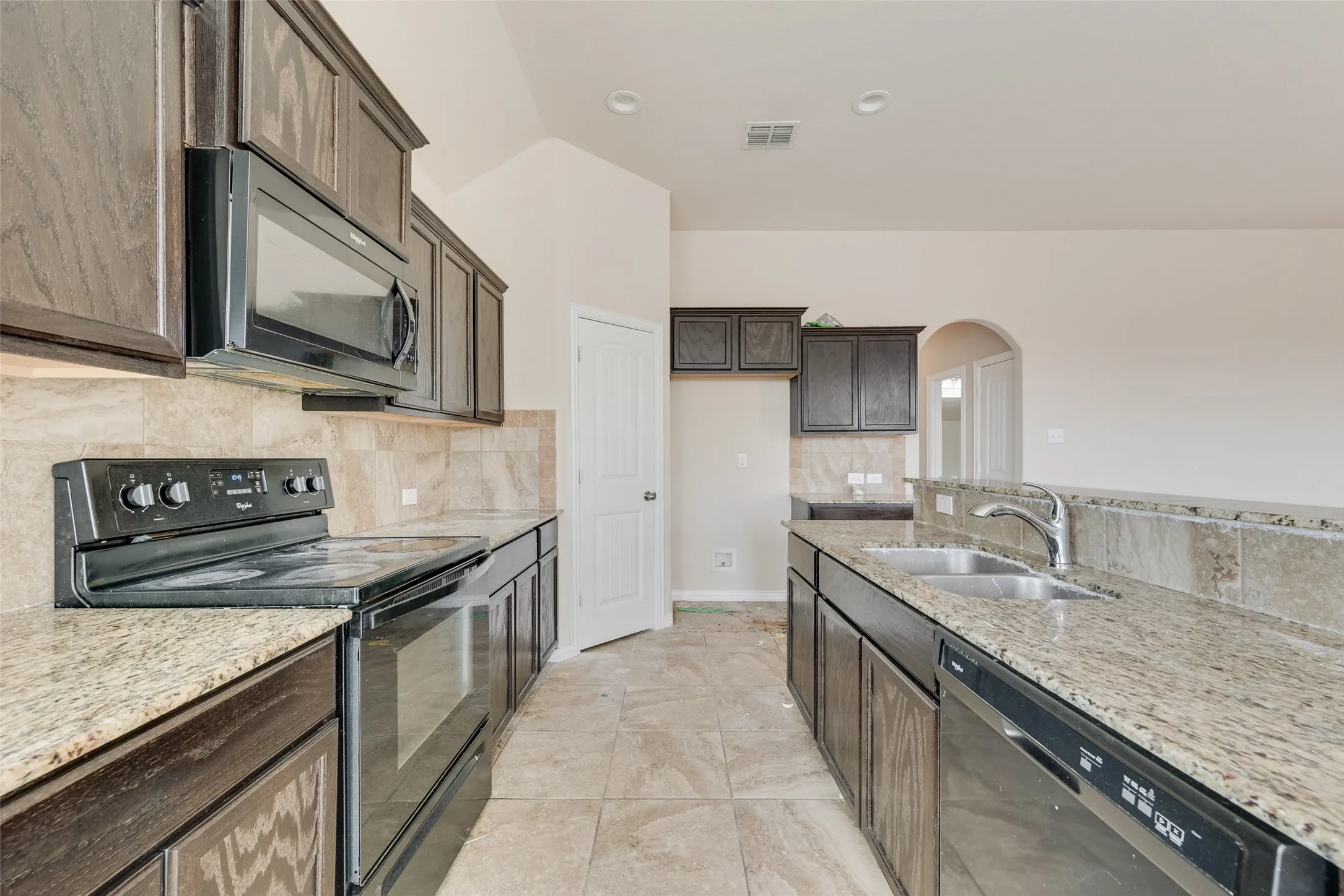 Kitchen featuring dark wood-finish cabinetry, granite countertops, tile backsplash, and a stainless steel double basin sink with a chrome faucet