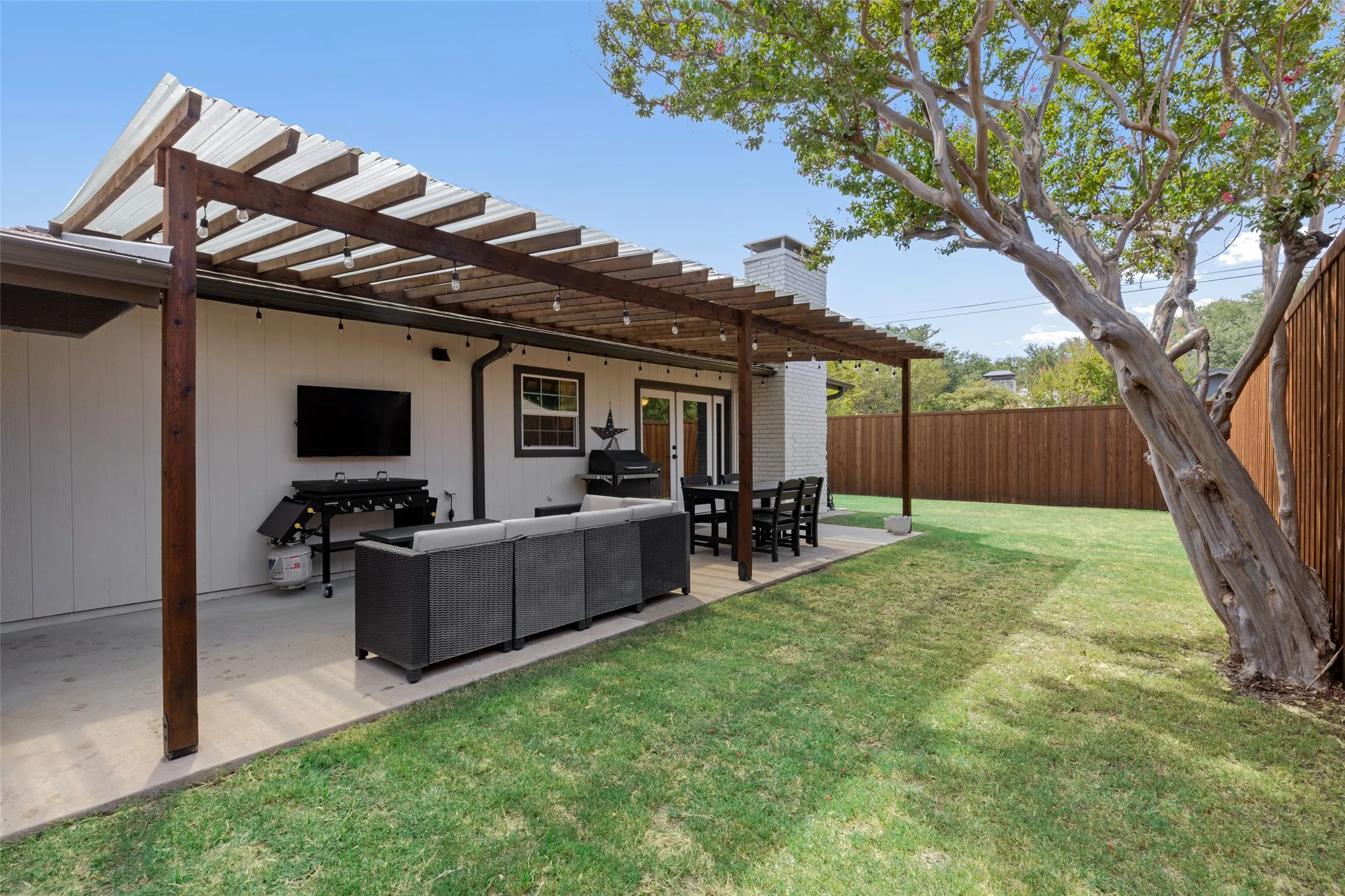 Privacy fencing wraps the full yard, with plenty of open grass beyond the covered patio.