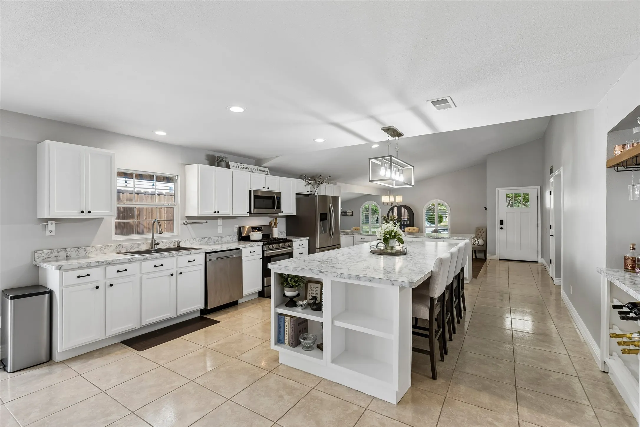White cabinetry and quartz-look counters run the full length of the kitchen, with sightlines clear to the front door.