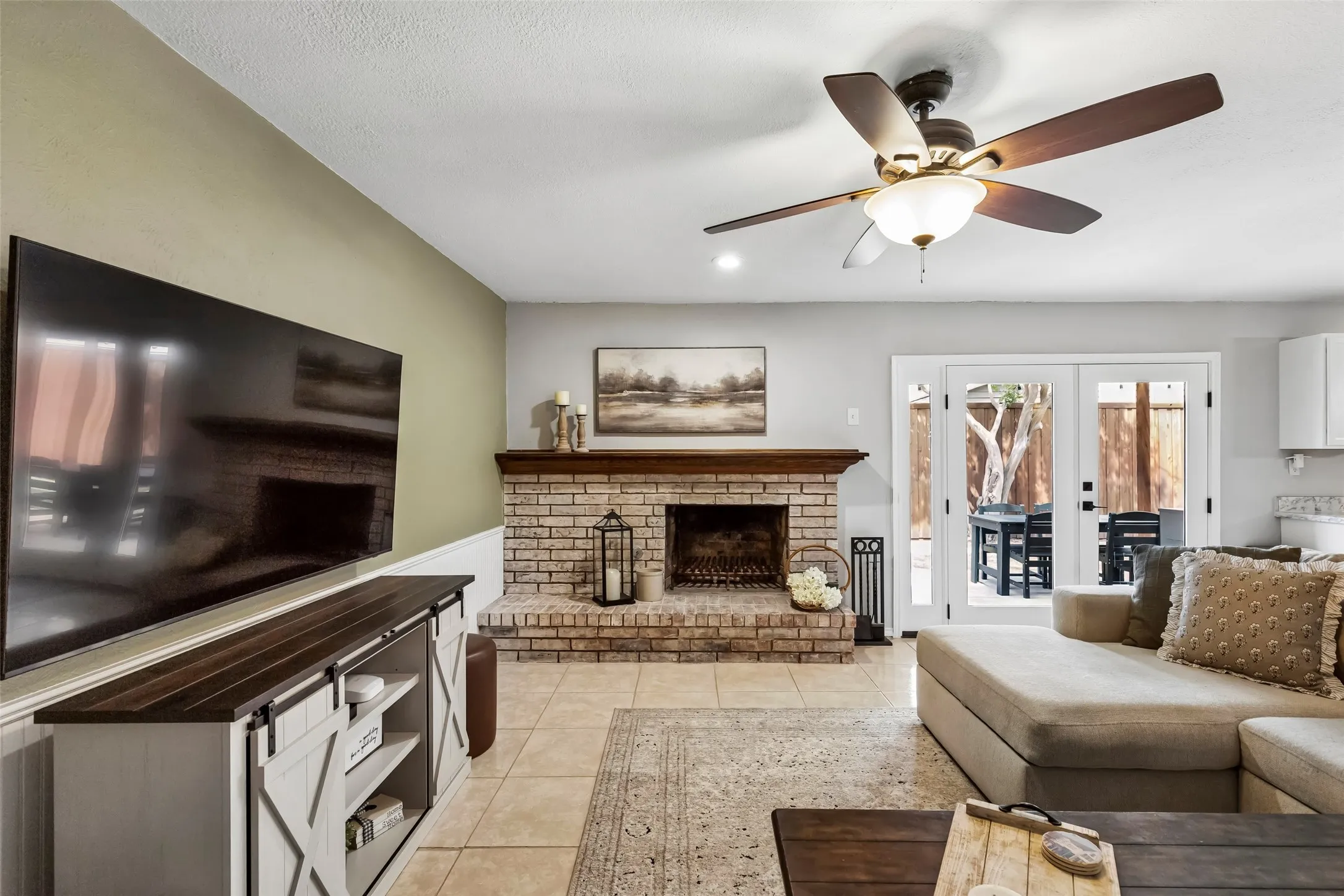 The living room's brick, wood-mantled fireplace sits open to the kitchen and dining room — all one continuous gathering space.