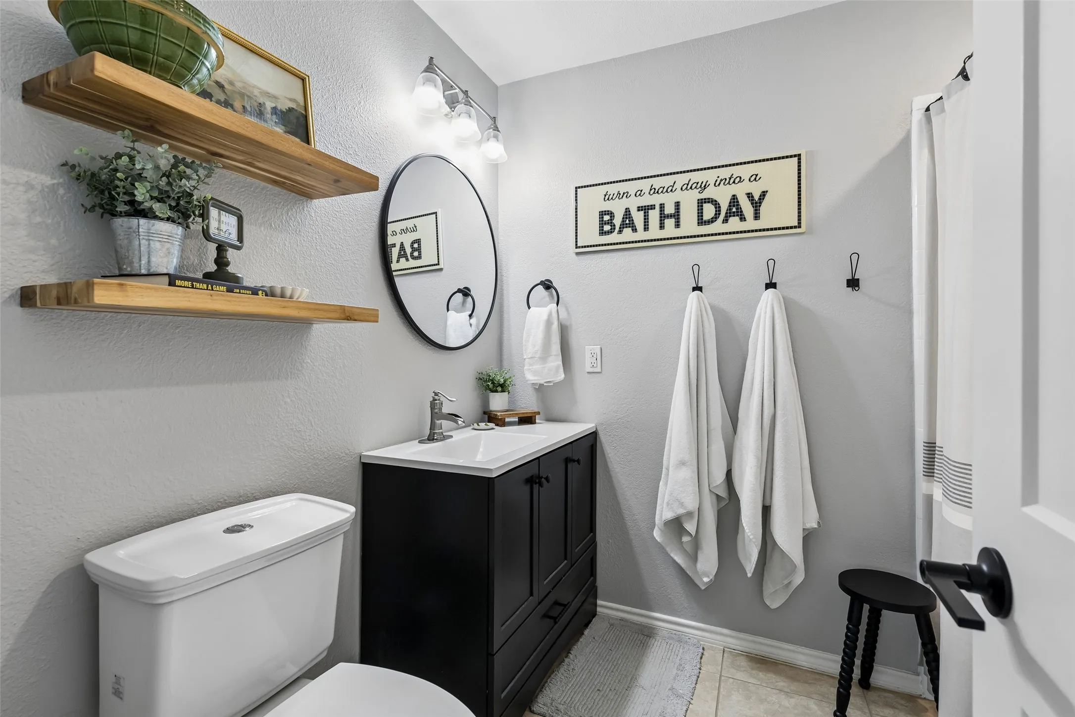 A round mirror and black hardware keep the hall bathroom's single vanity simple and functional.