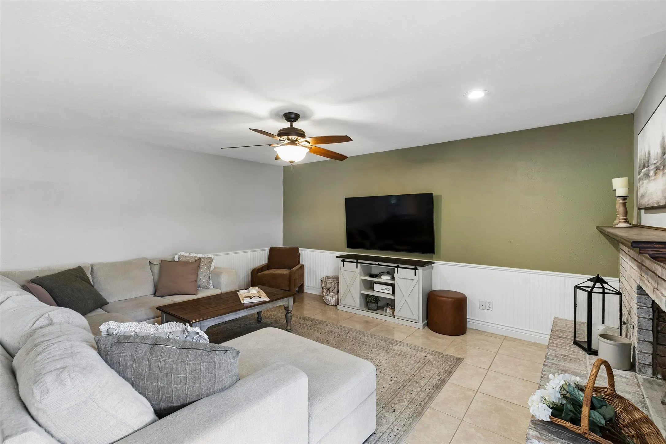 A soft green accent wall pairs with the brick fireplace for an easy, low-key living room feel.
