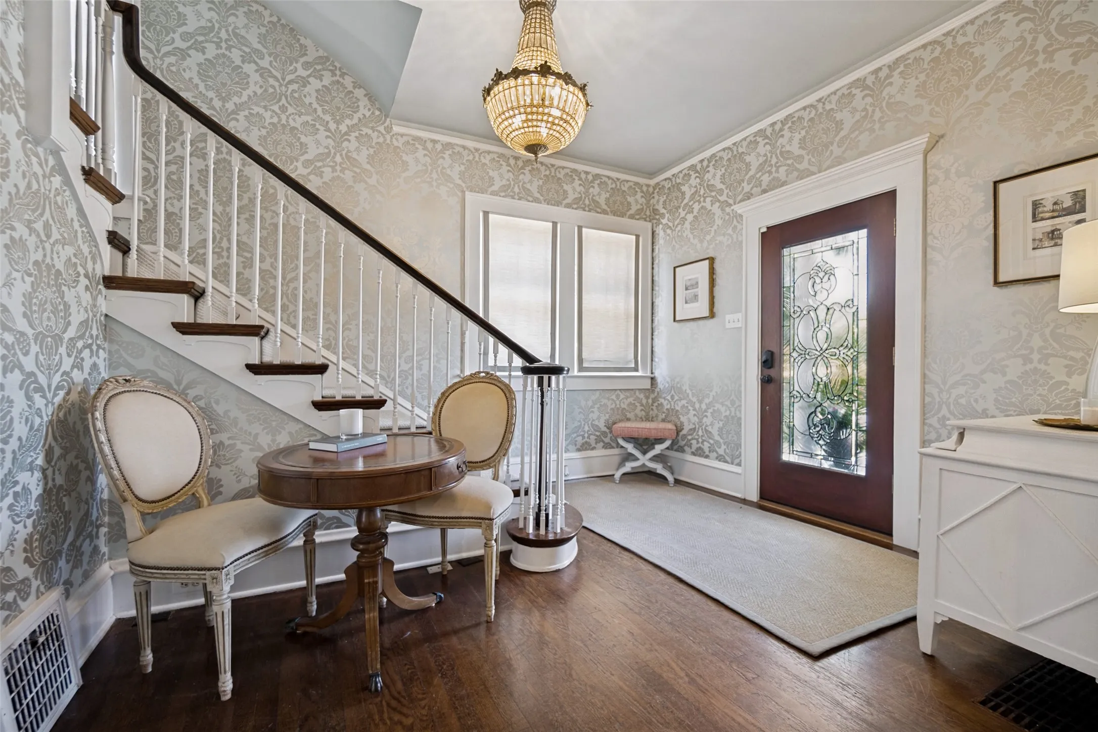 Ornate chandelier, wood-finish flooring, staircase with white balusters, decorative wall covering, and a front door with leaded glass