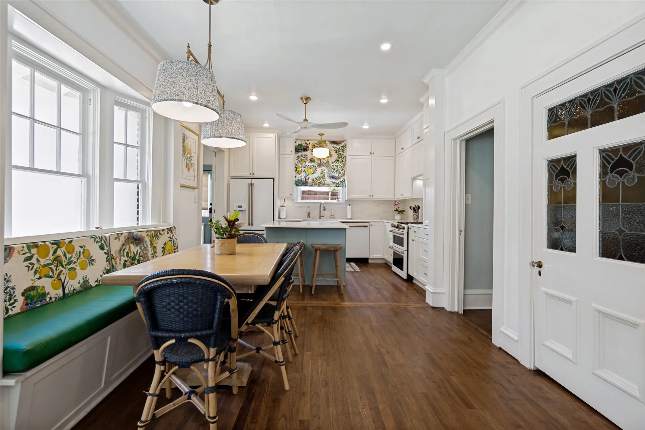 Hardwood flooring, built-in banquette seating with storage, white cabinetry, kitchen island, and stained-glass door