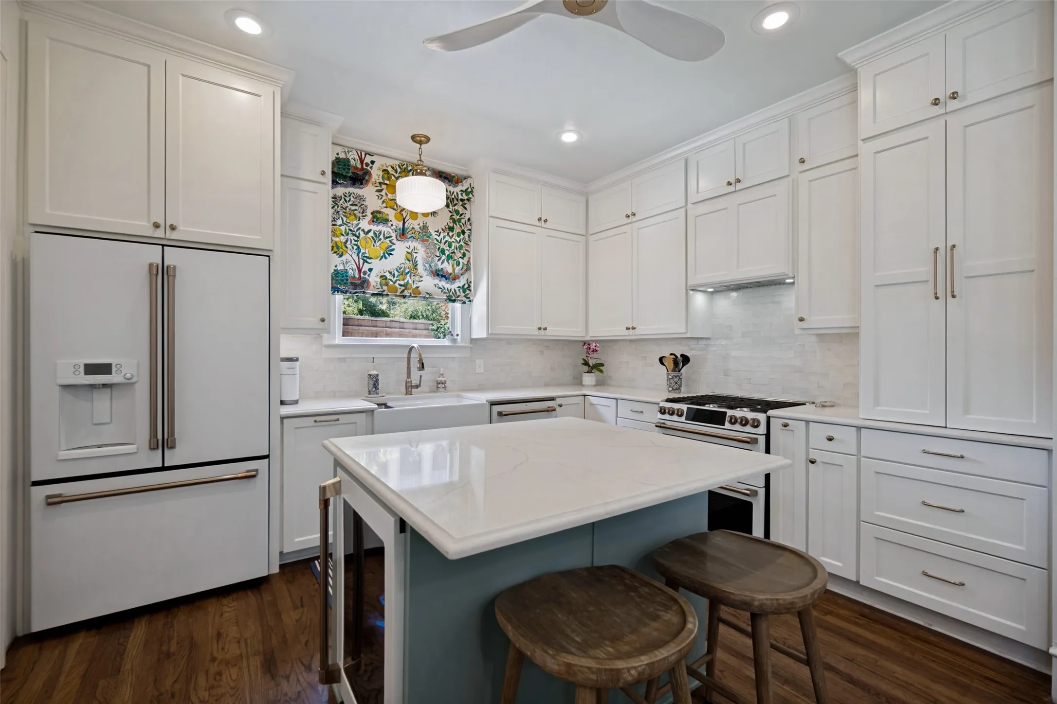 Crisp white cabinetry, wood-finish flooring, central island with seating, stainless steel appliances, and recessed lighting