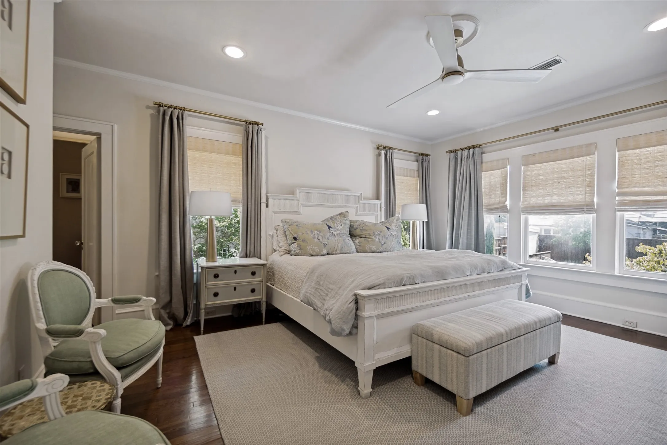 Recessed ceiling lighting, a modern ceiling fan, wood-finish flooring, and multiple windows with window treatments
