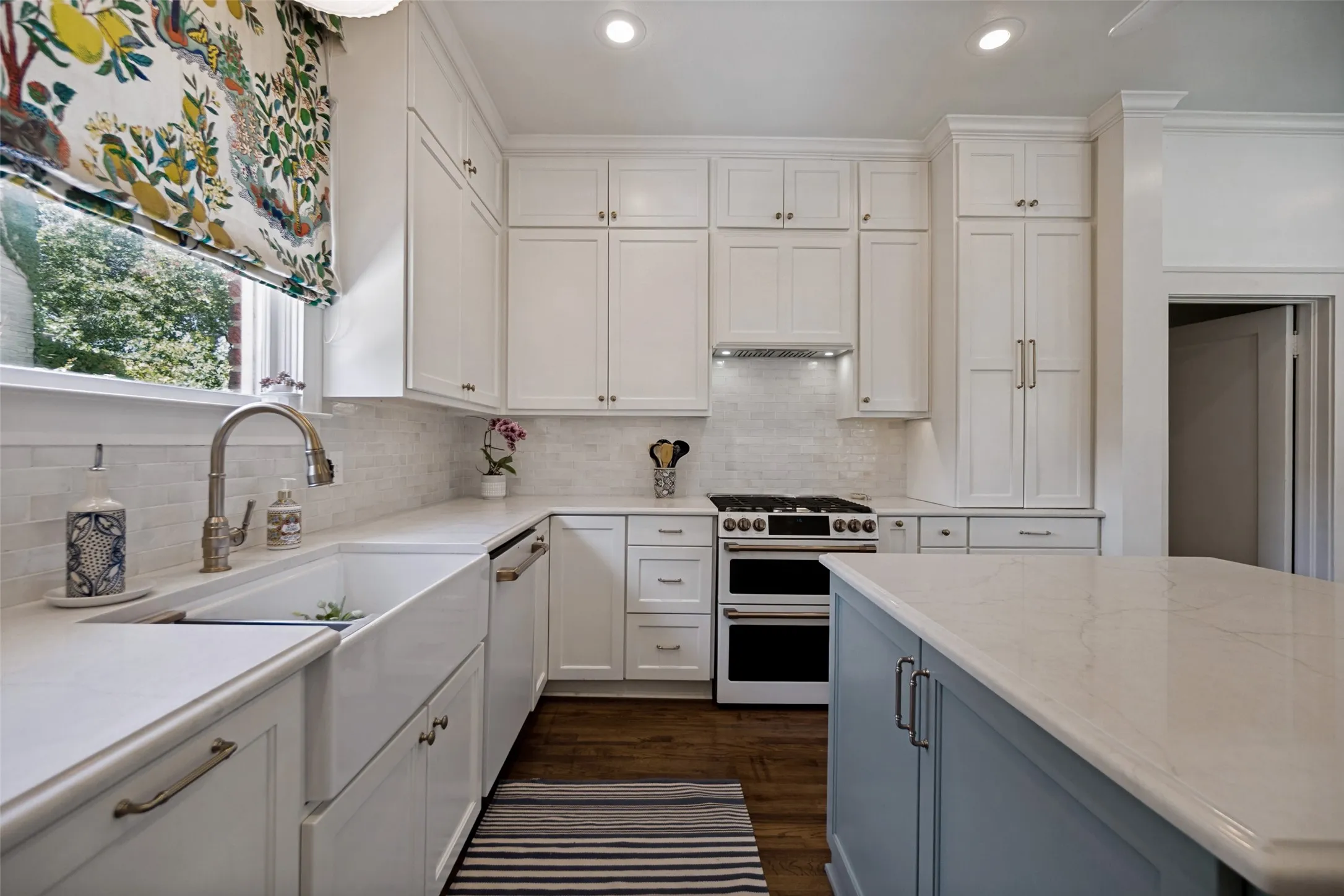 White cabinetry with brushed nickel hardware, expansive countertop space, white subway tile backsplash, farmhouse-style sink, and wood-finish flooring