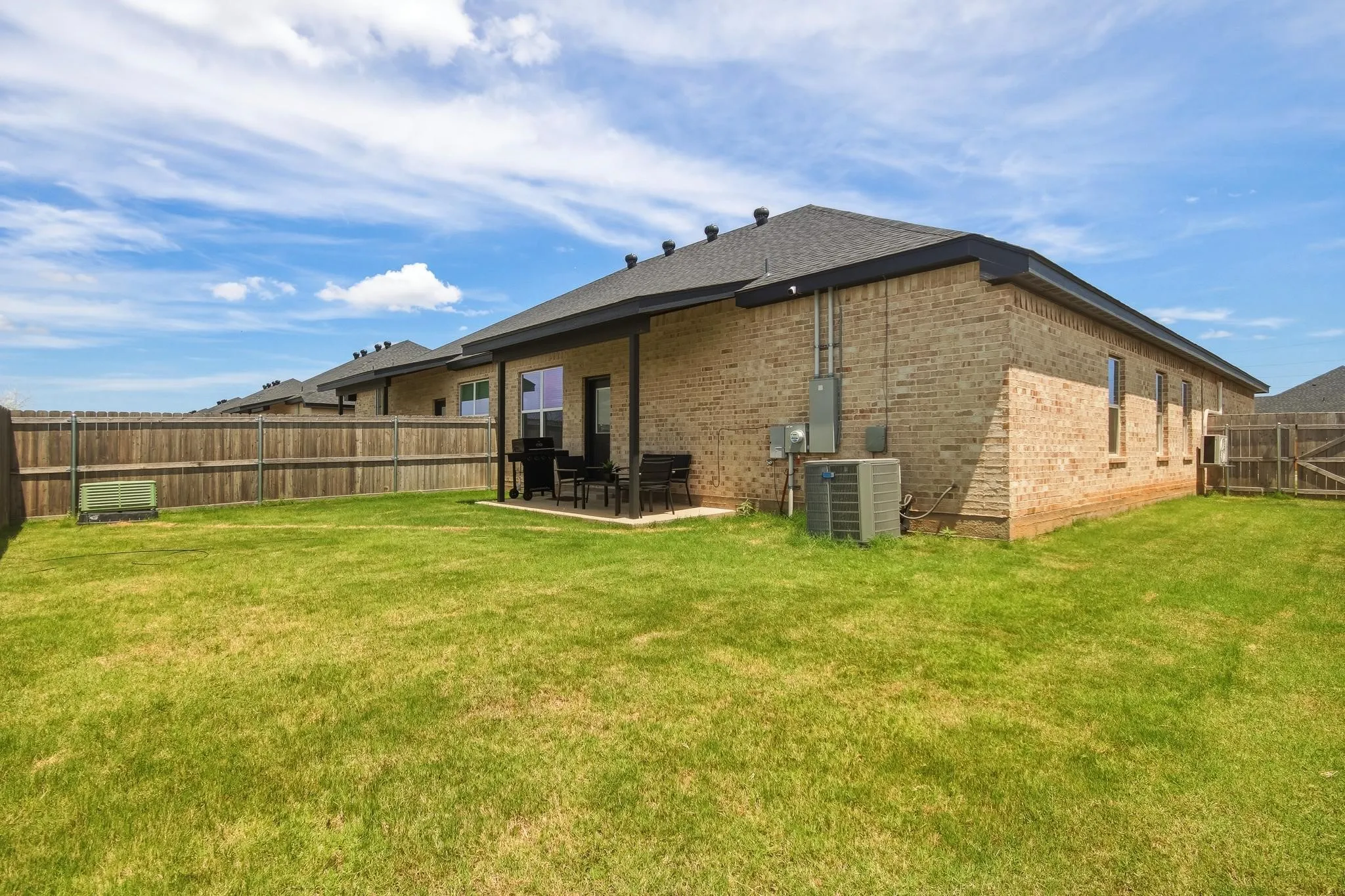 Brick exterior with dark shingle roof, covered patio, and wood privacy fencing