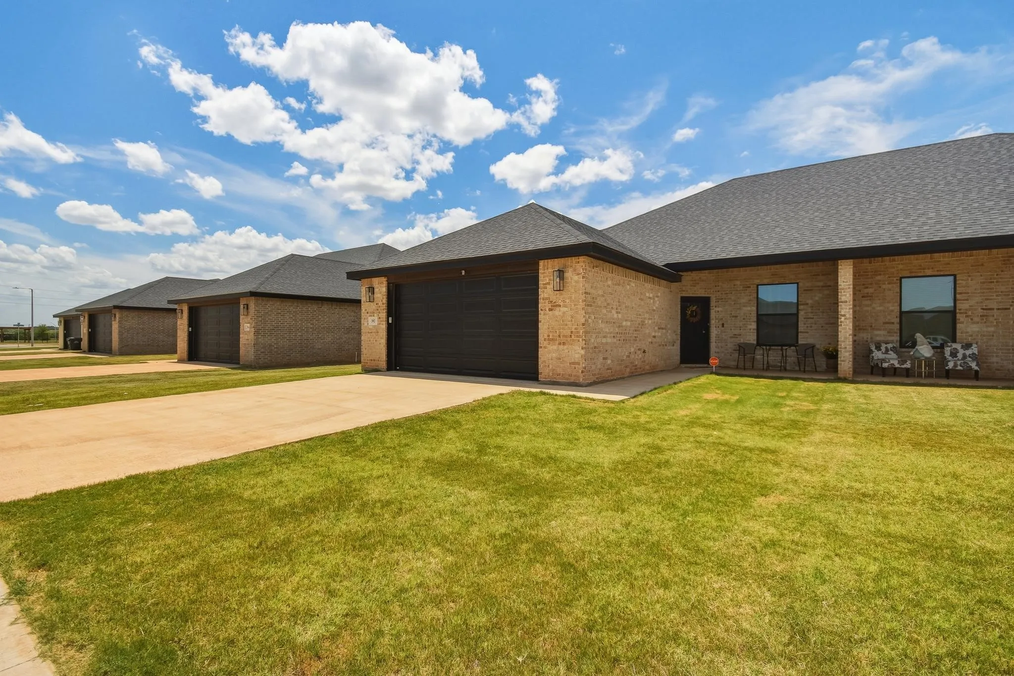 Brick exterior with dark shingle roofing, integrated garage, and a covered front porch