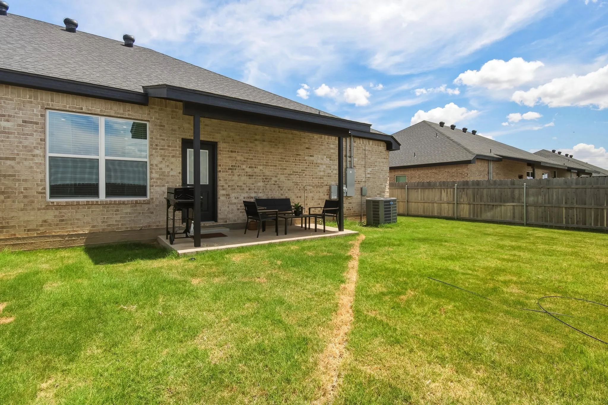 Expansive backyard featuring a covered patio, brick exterior, wood fence, and a large grassy area