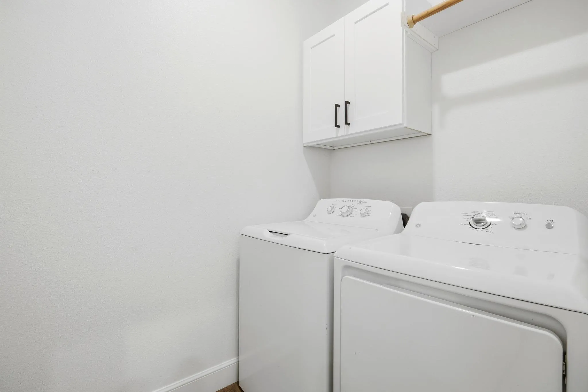 Laundry area featuring overhead cabinetry with black hardware and a wooden hanging rod