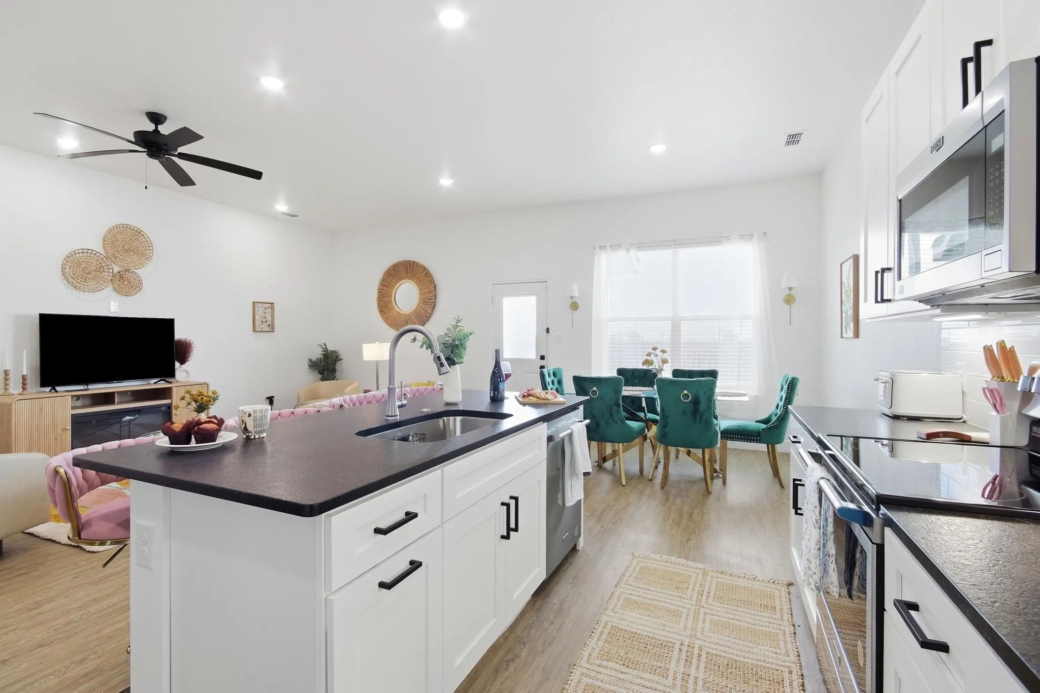 Open-concept living area featuring a kitchen island with sink, white cabinetry with black hardware, stainless steel appliances, and wood-finish flooring