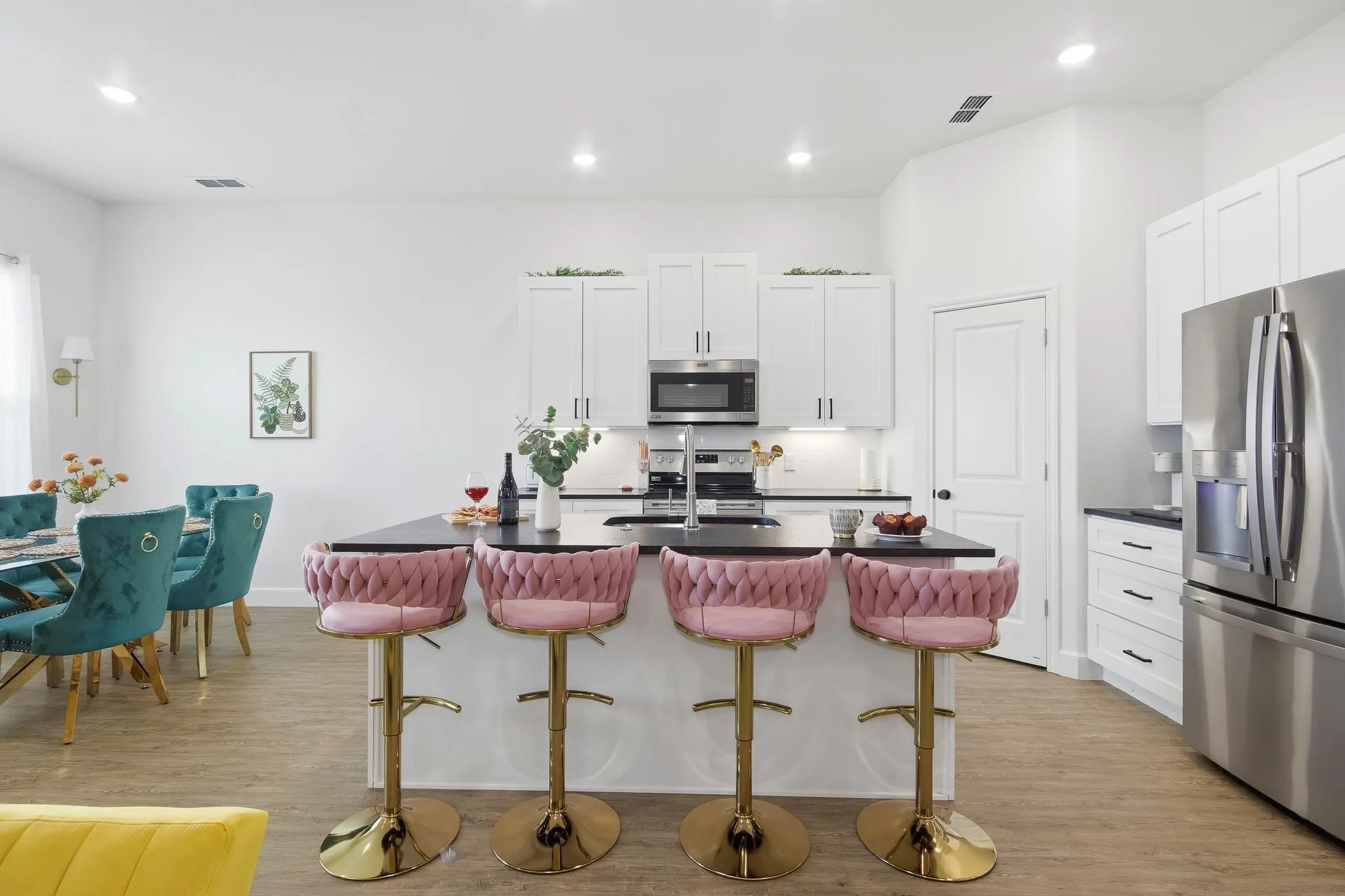 Open-concept kitchen featuring an island with built-in sink, stainless steel appliances, white cabinetry, and wood-finish flooring