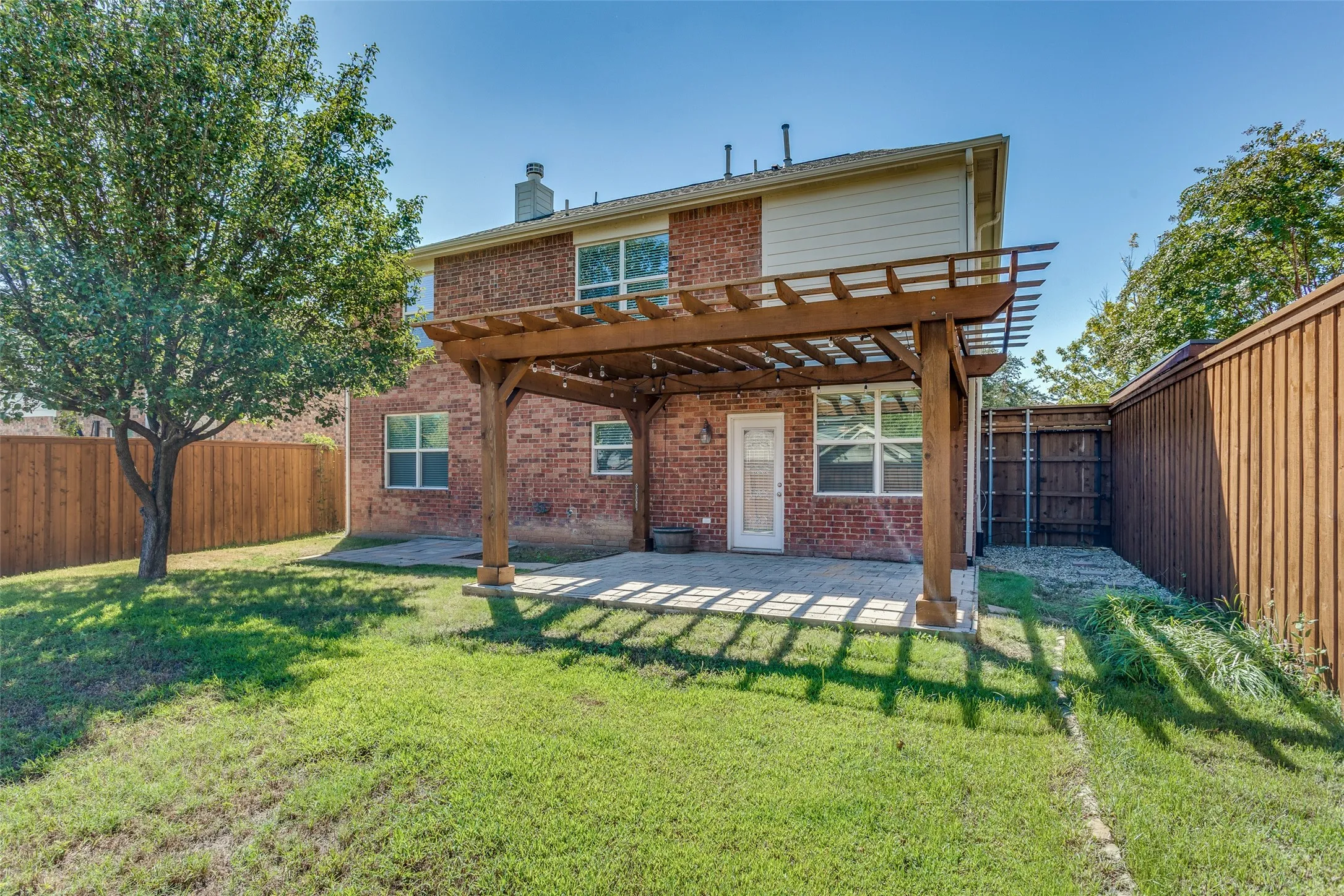 Backyard has features a board on board fence as well as wooden pergola covering a patio.