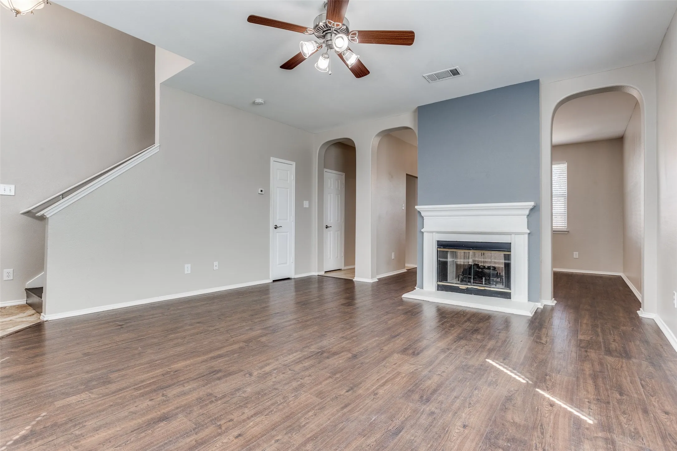 Spacious living area featuring wood-finish flooring, a white mantel fireplace, and arched doorways