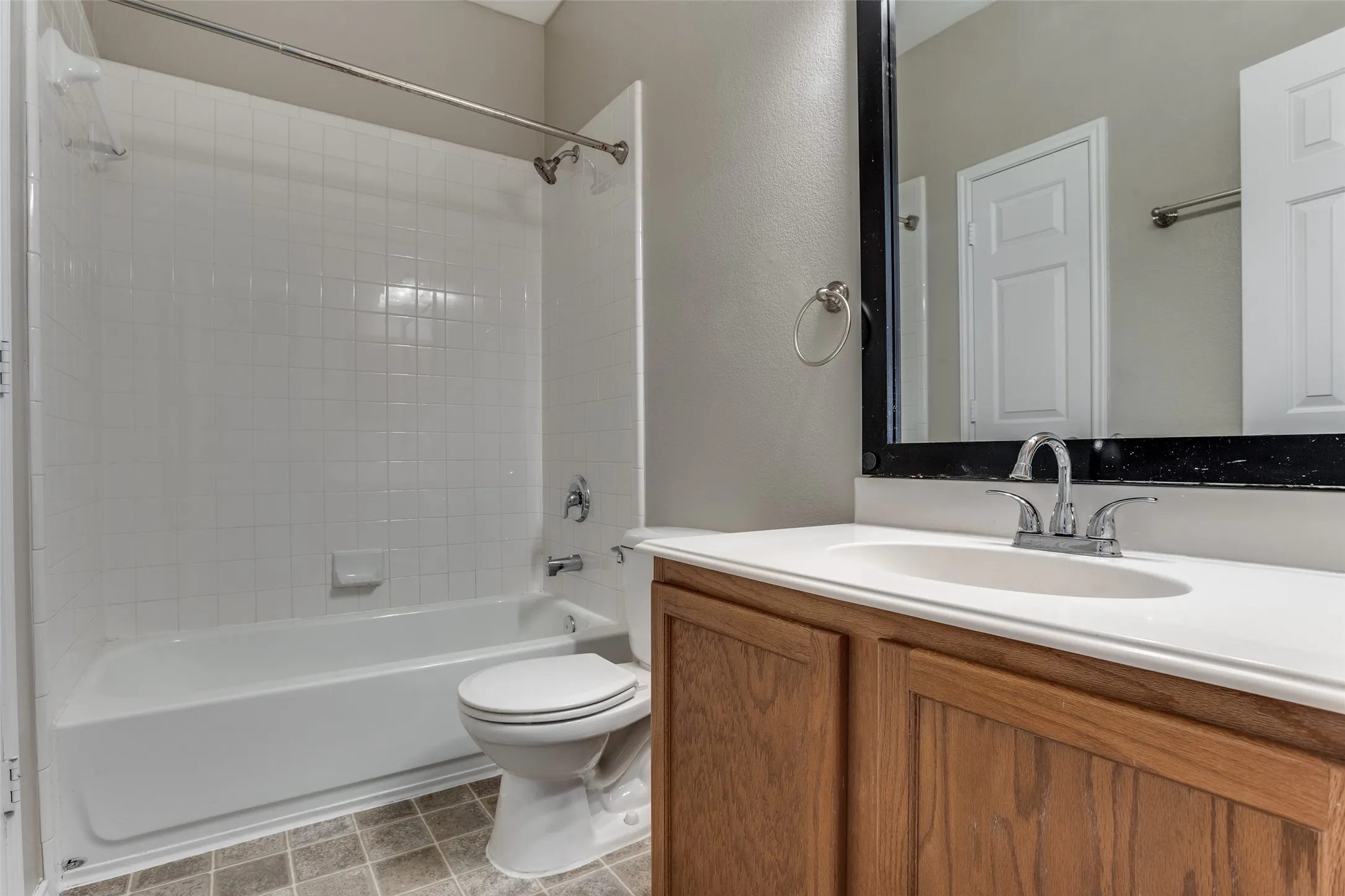 Bathroom featuring a single vanity with wood-finish cabinetry, a framed mirror, and a shower-over-tub combination.