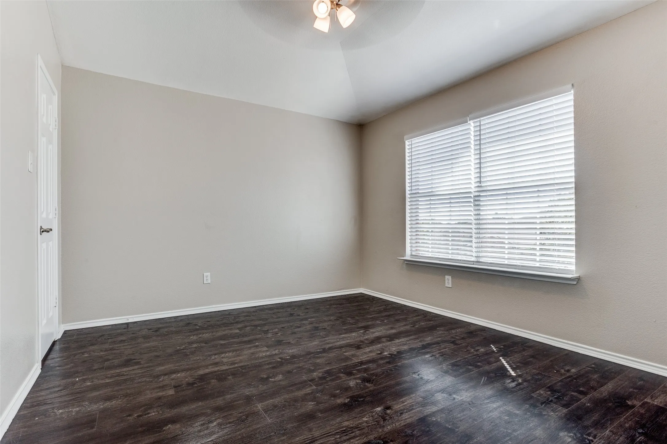 Spacious room featuring wood-finish flooring, light-toned walls, and a ceiling fan.