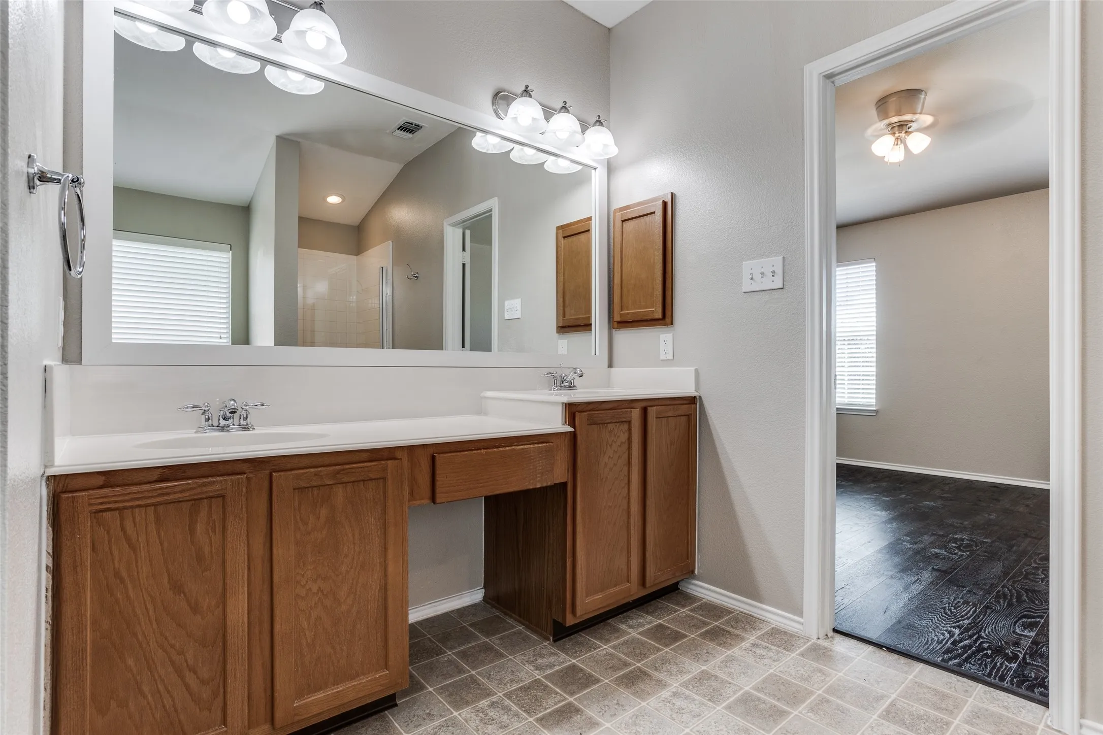En suite bathroom vanity featuring dual sinks, overhead lighting, wood-finish cabinetry, built-in storage, and a separate vanity area