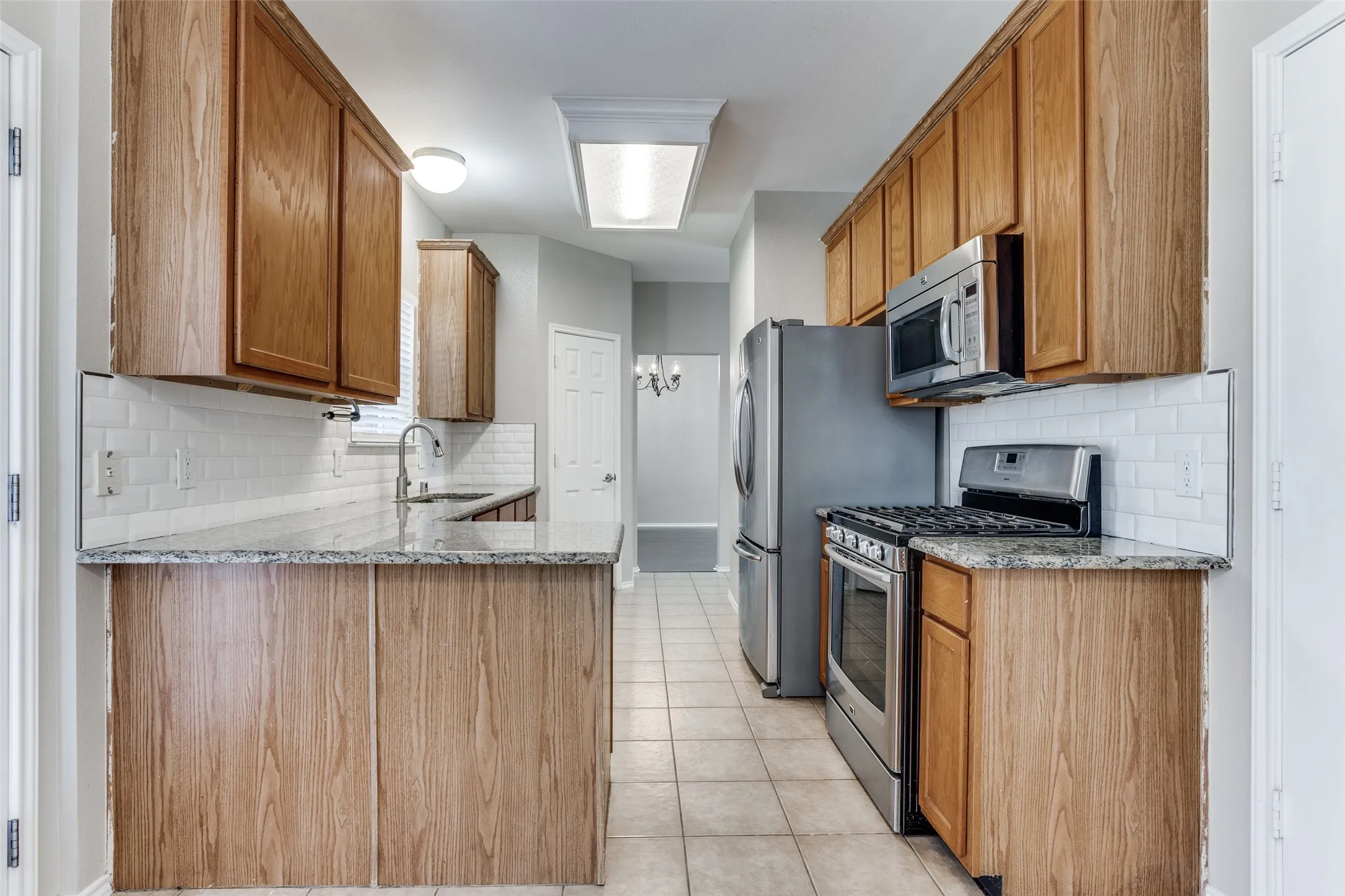 Kitchen featuring granite countertops, wood cabinetry, stainless steel appliances, white subway tile backsplash, and tile flooring