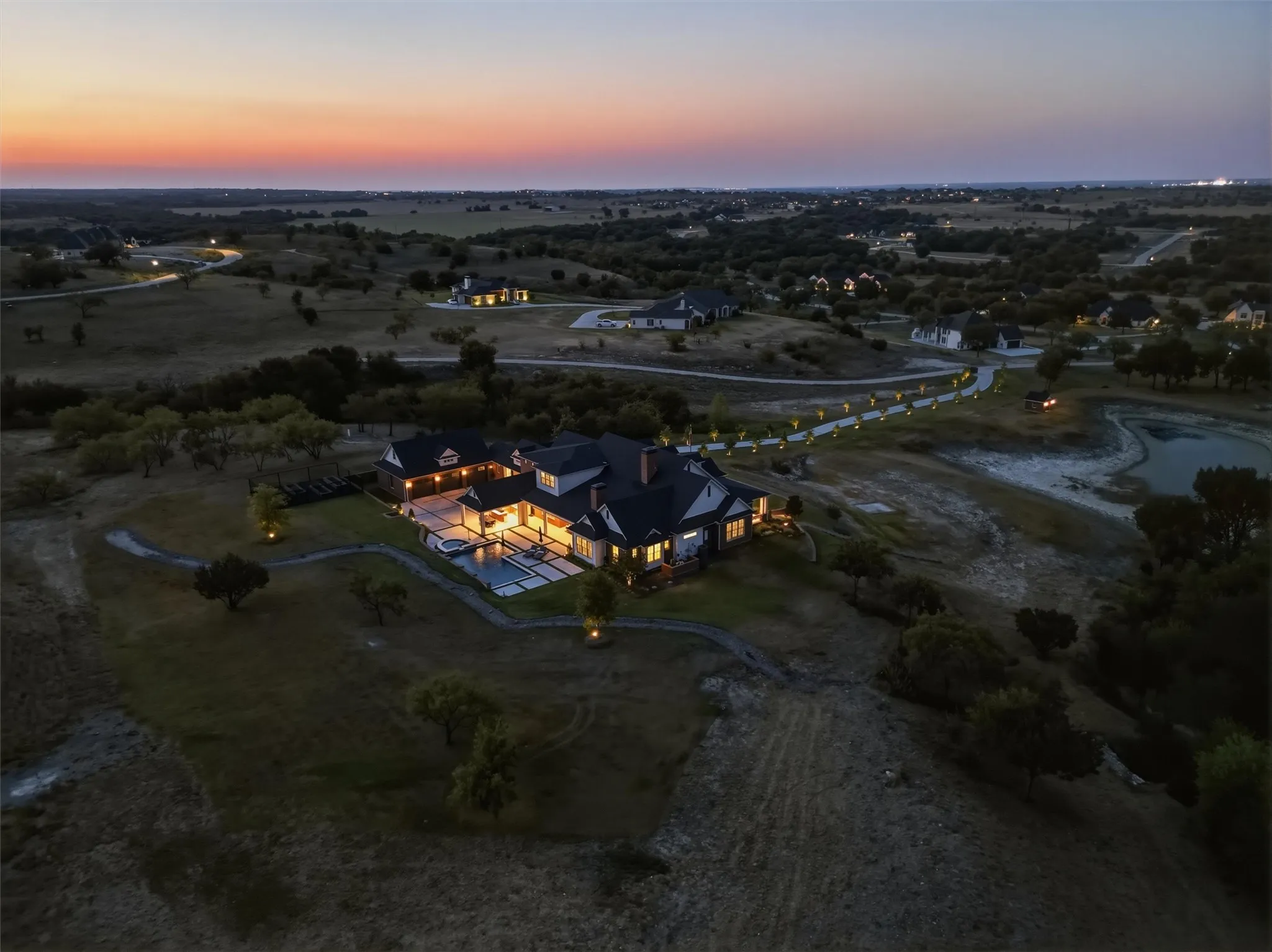 This aerial view shows you the beautiful sunset with the back of the home lit up. Notice the long oak-lined driveway and private pond.