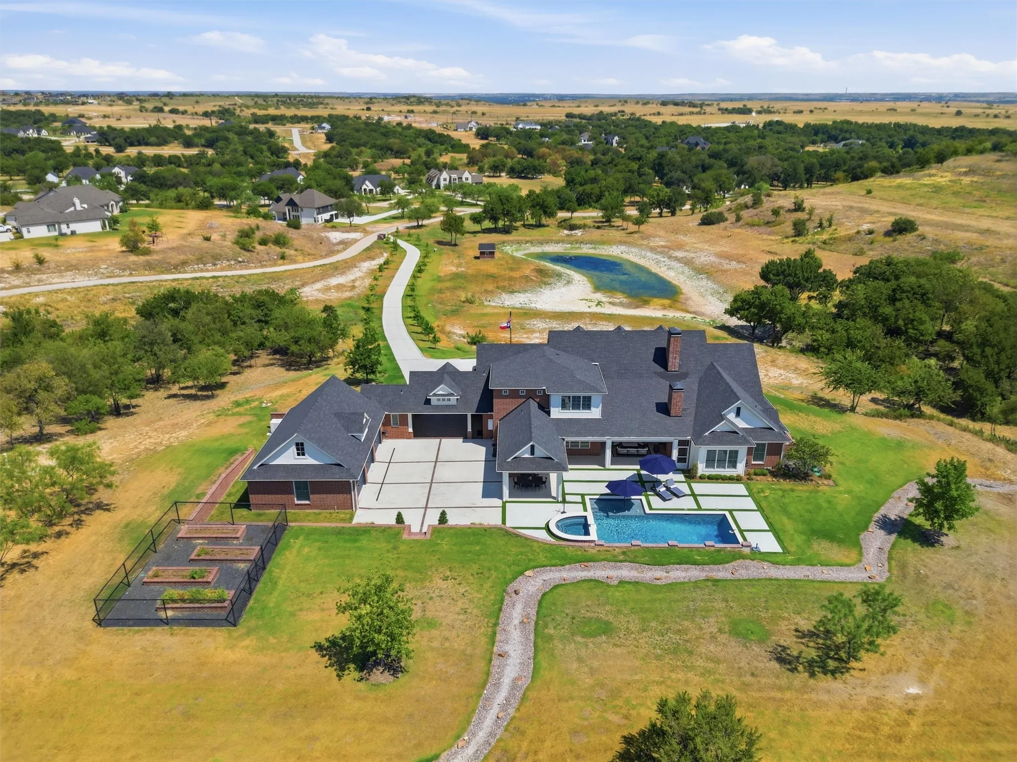 This is the perfect view of the long oak lined driveway. The front porch overlooks the private pond. You can see the three car garage leading into the outdoor living area. The outdoor living area offers a large covered back patio, outdoor kitchen, covered dining, and garden.