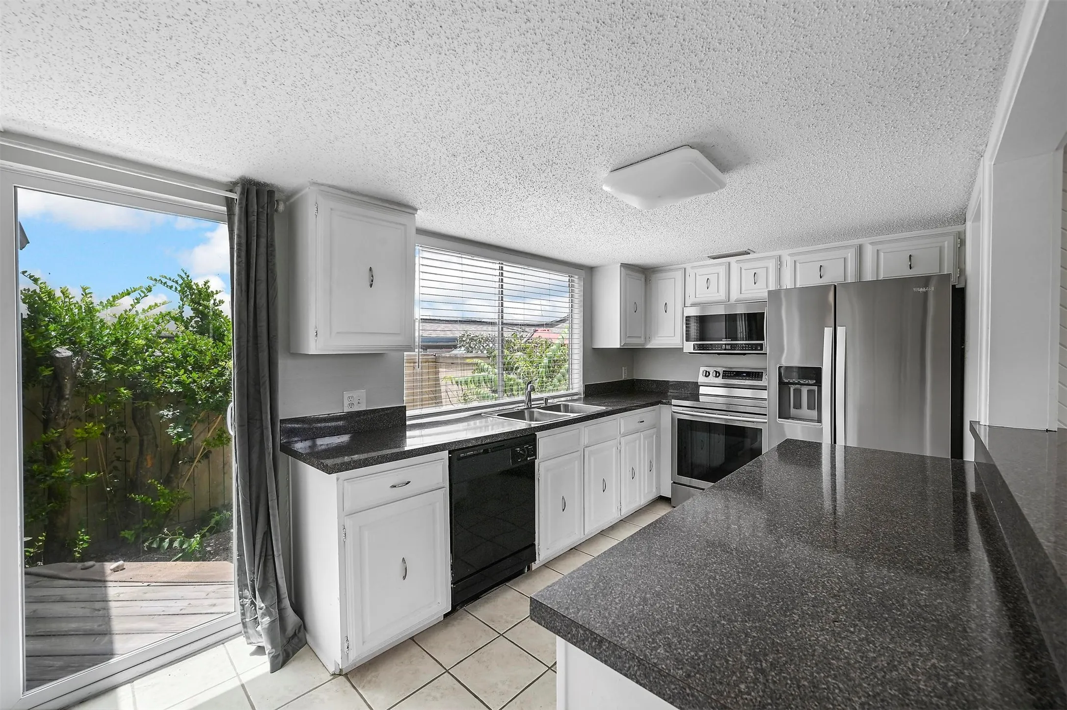 Kitchen with stainless steel appliances, white cabinets, sink, a textured ceiling, and light tile patterned flooring