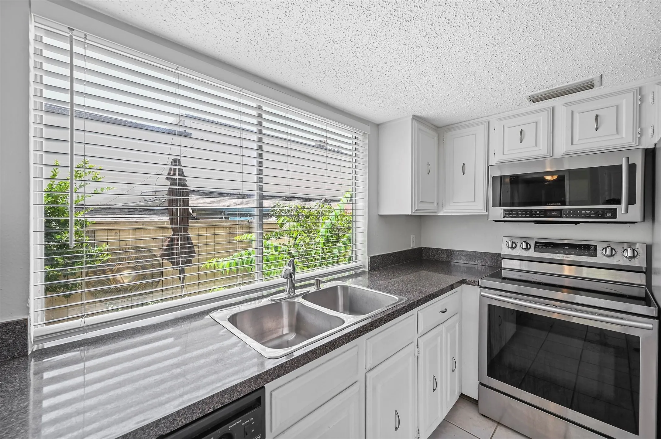 Kitchen featuring light tile patterned flooring, white cabinetry, a textured ceiling, stainless steel appliances, and sink