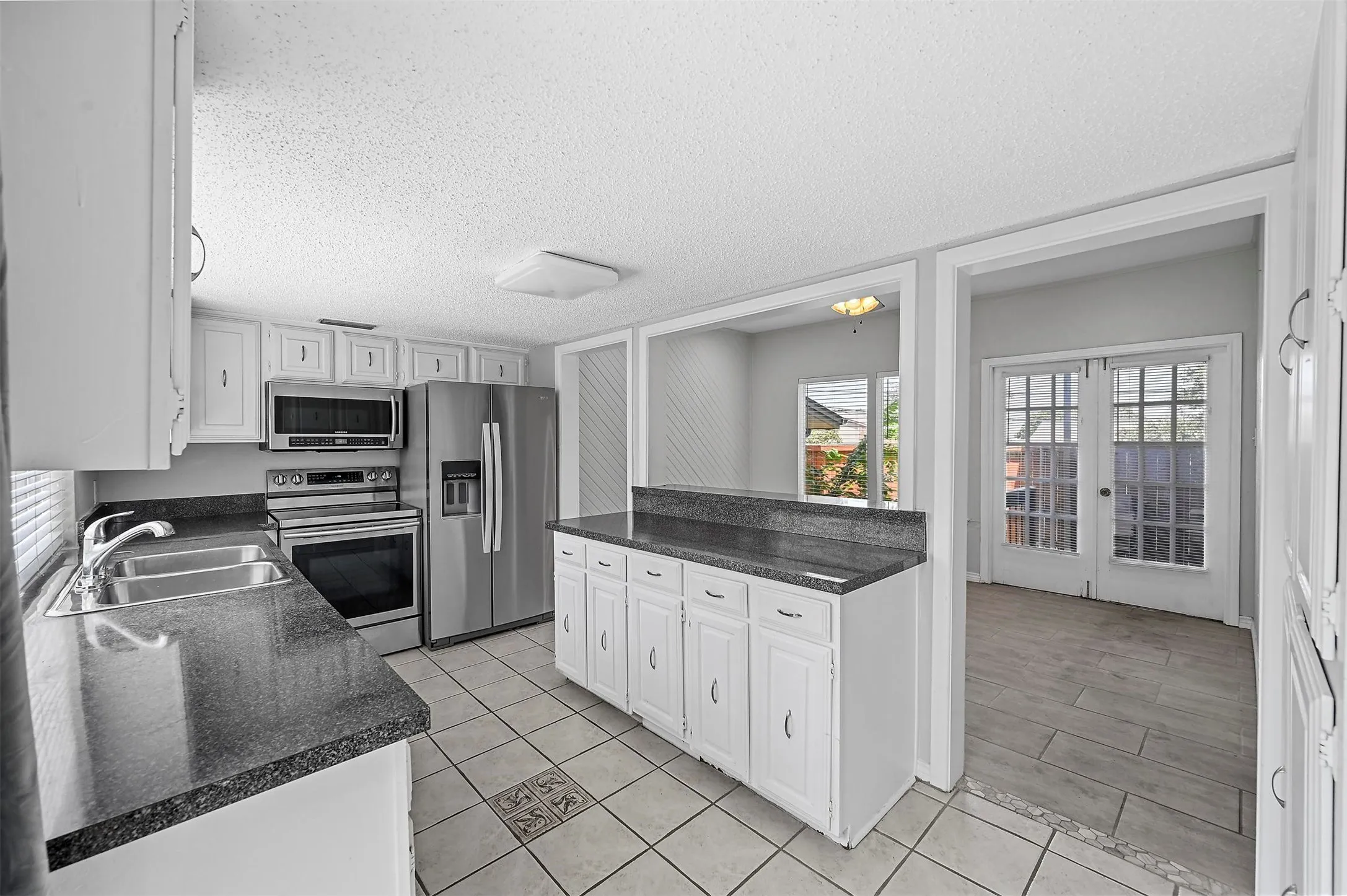 Kitchen with appliances with stainless steel finishes, sink, light tile patterned floors, a textured ceiling, and white cabinetry
