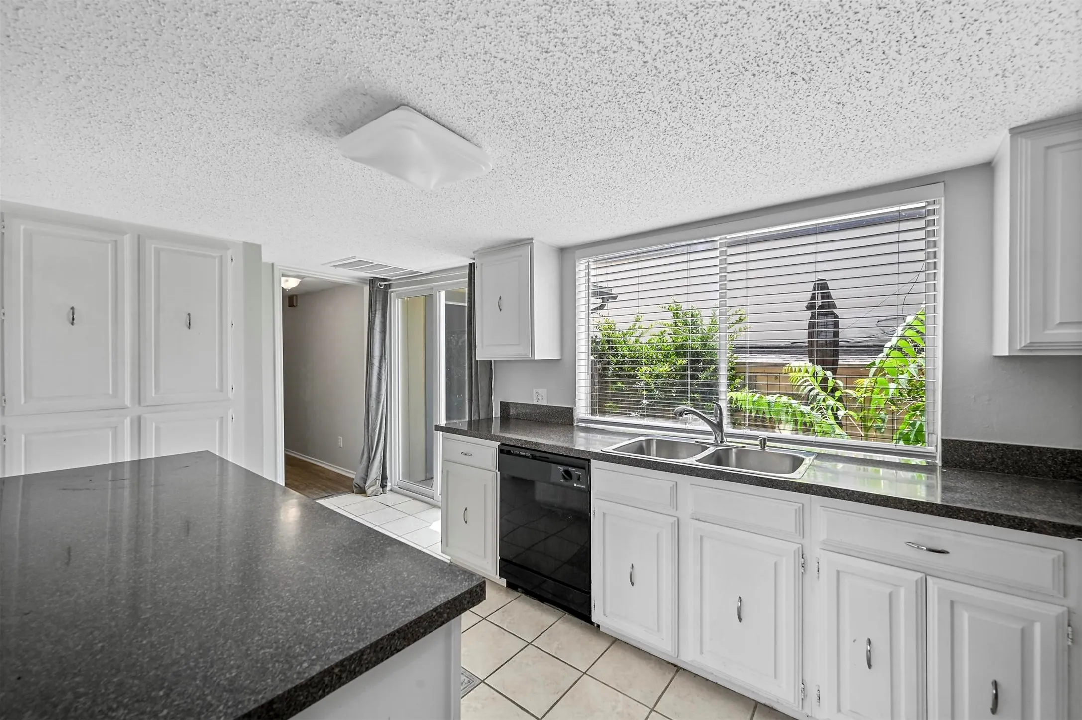 Kitchen with black dishwasher, sink, light tile patterned floors, and white cabinetry