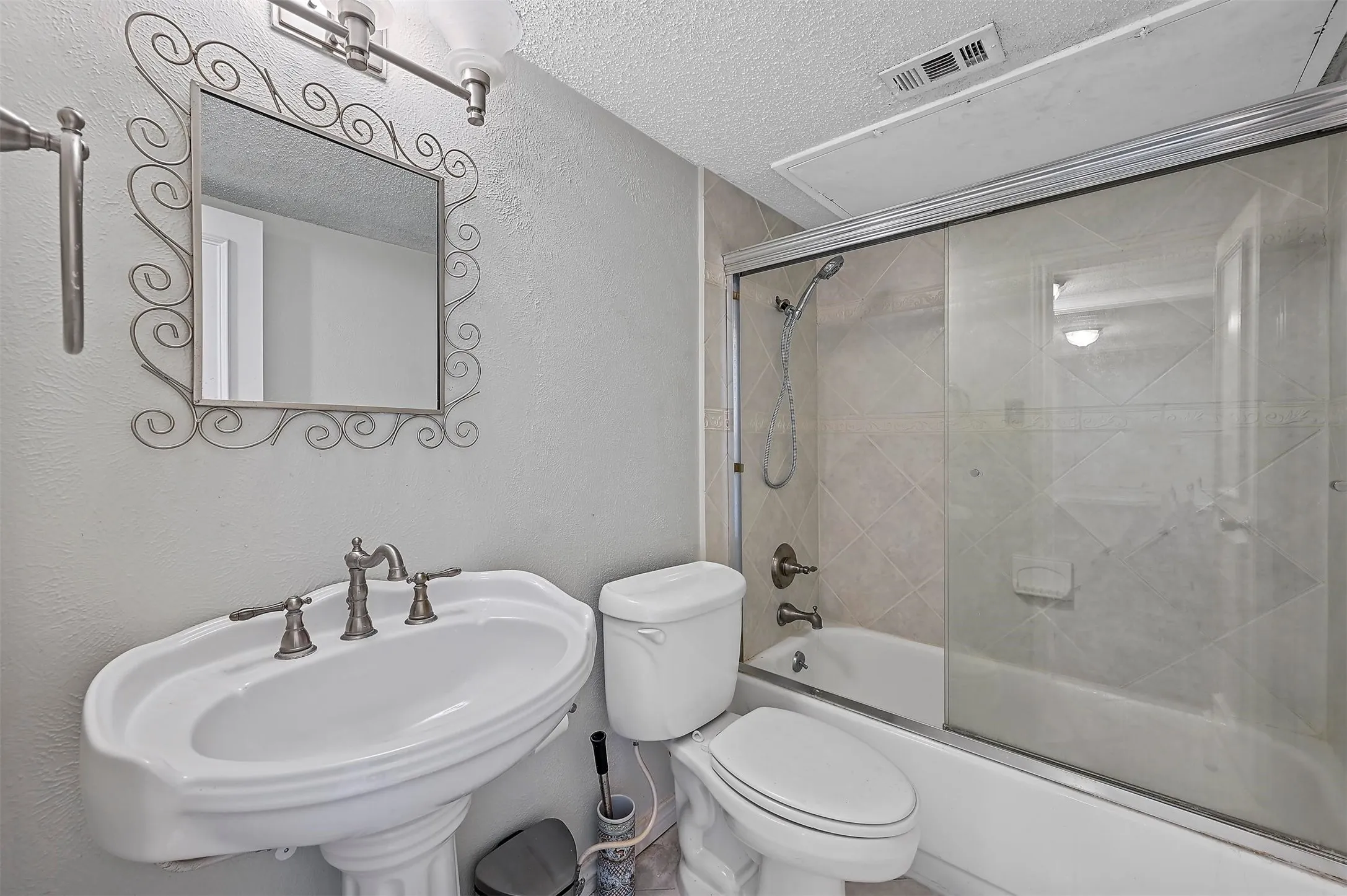 Full bathroom featuring combined bath / shower with glass door, sink, a textured ceiling, and toilet