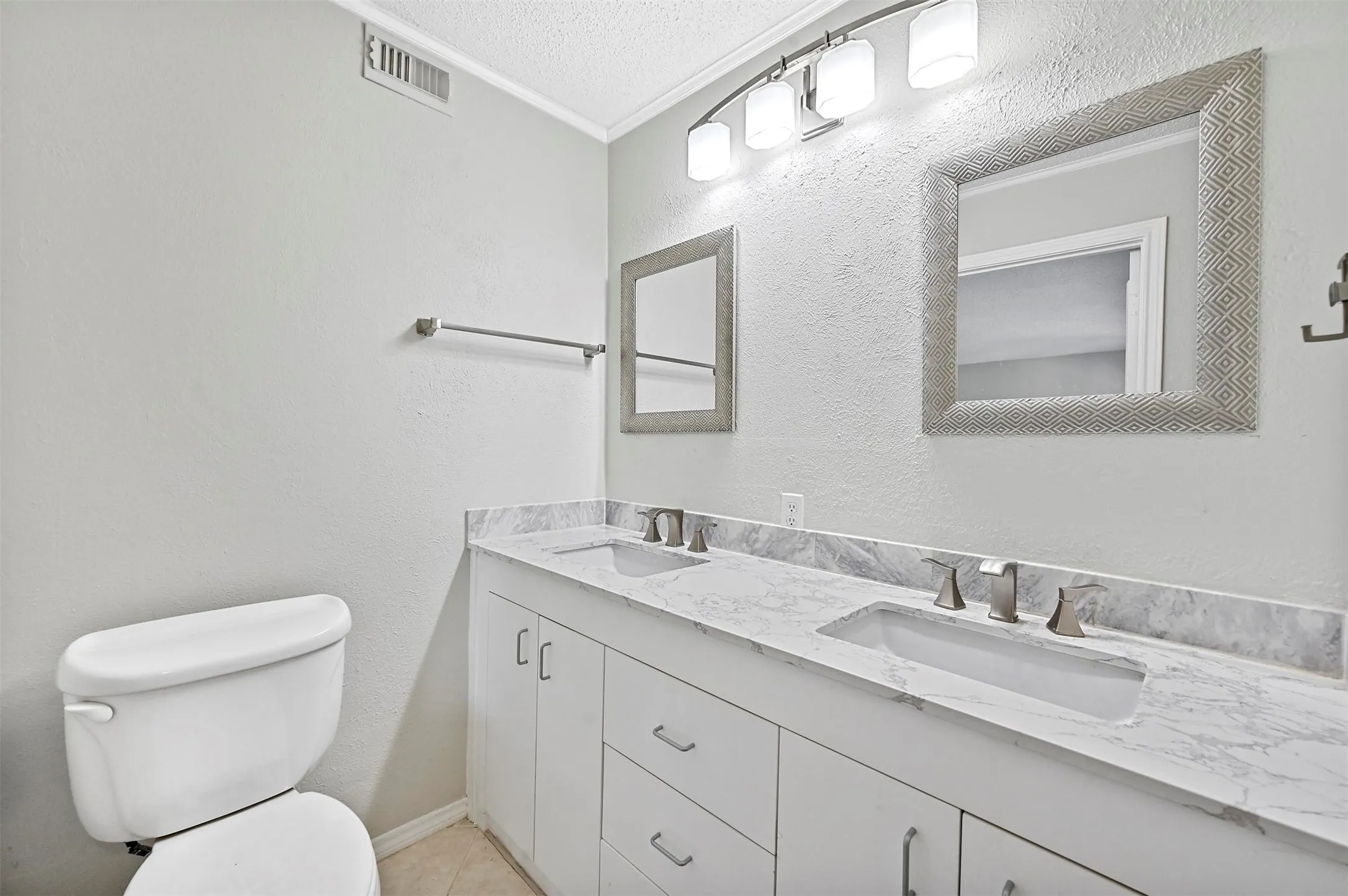 Bathroom featuring dual vanity, crown molding, toilet, and a textured ceiling
