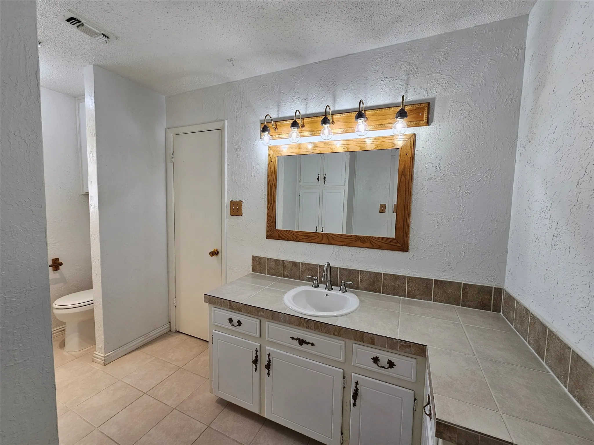 Vanity with integrated sink, tile countertop, and wood-framed mirror