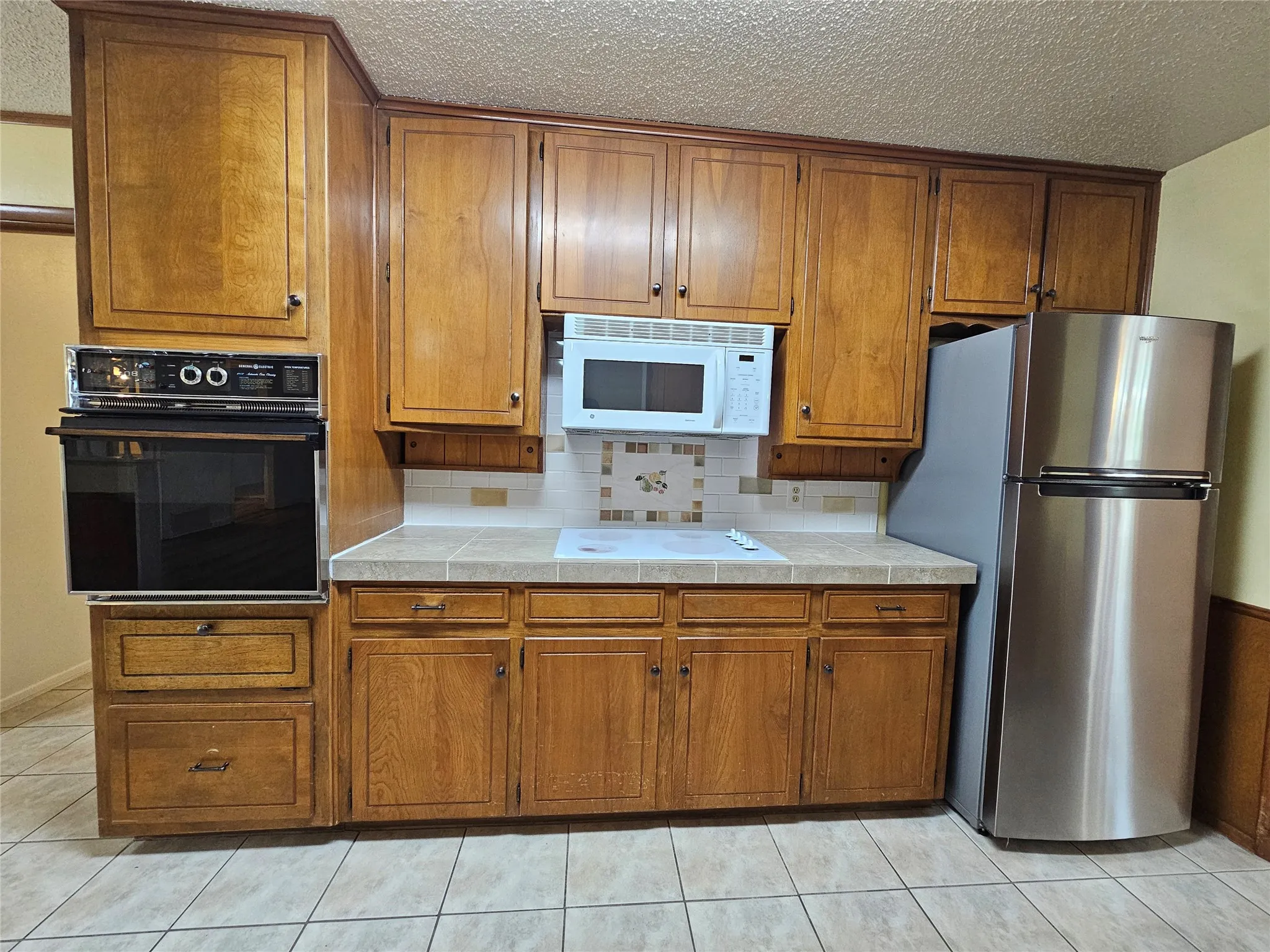 Wood-finish cabinetry, tile flooring, built-in oven, stainless steel refrigerator, and microwave