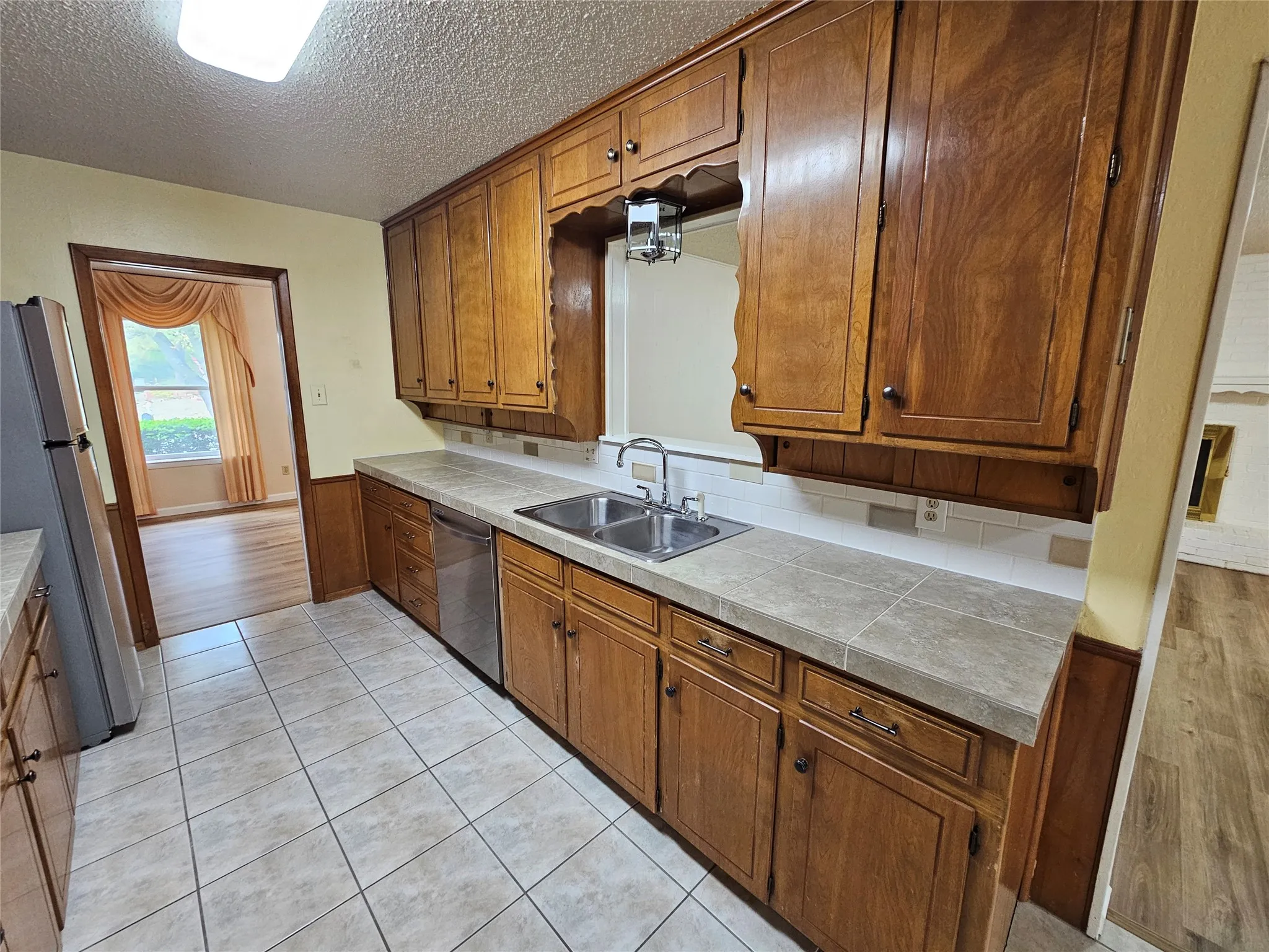 Kitchen featuring wood cabinetry, a dual basin stainless steel sink, tile countertops, a white subway tile backsplash, and tile flooring