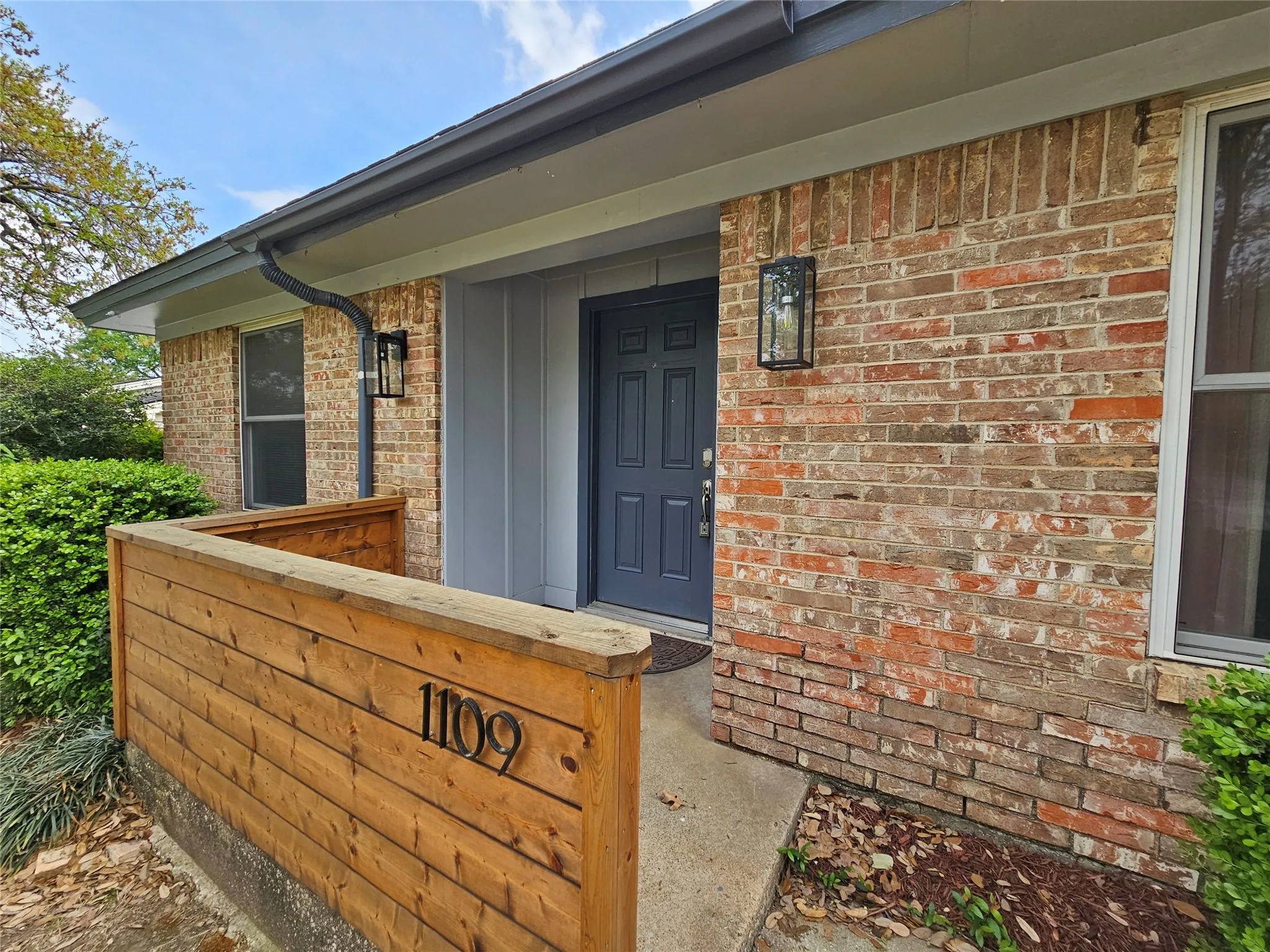 Brick facade with contrasting dark trim, dark entry door, and two exterior wall sconces