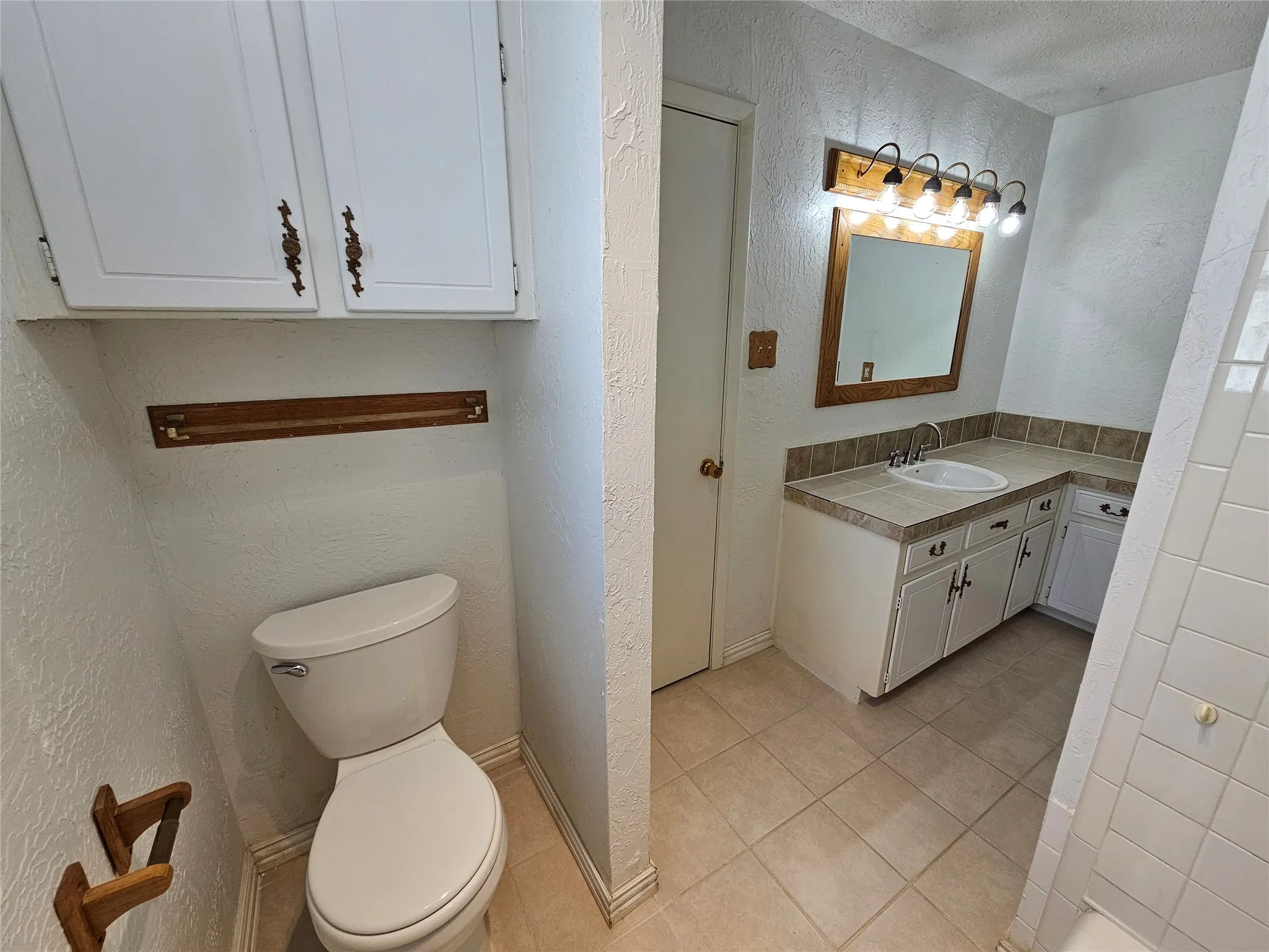 Built-in vanity with integrated sink, tile countertop, and mounted mirror with overhead lighting
