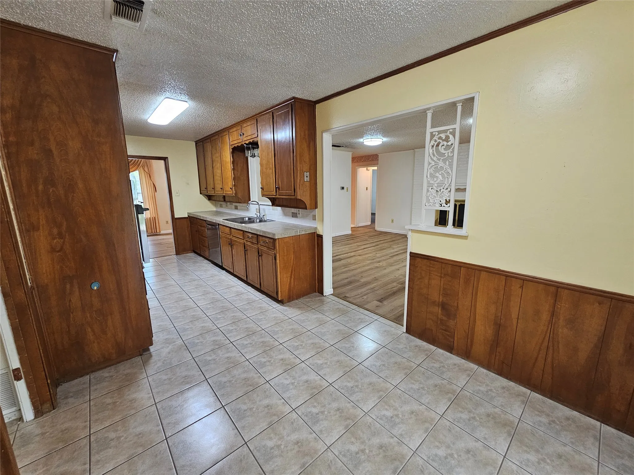 Tile flooring and paneling detail in the kitchen, featuring wood cabinetry, stainless-steel sink, and a built-in dishwasher