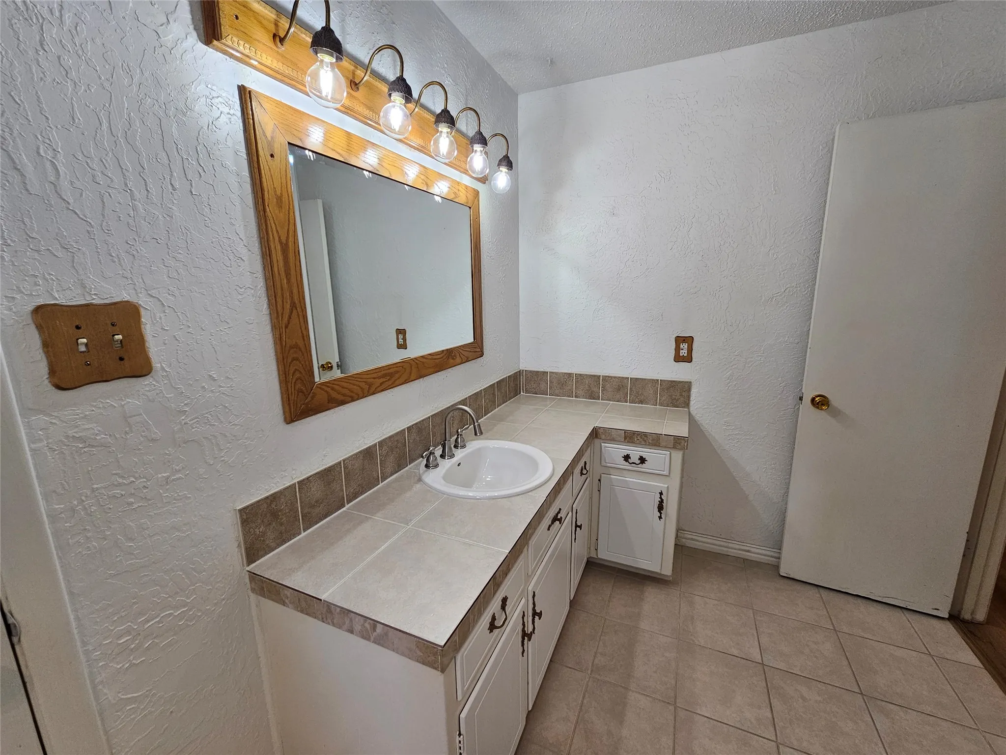 White vanity with a drop-in sink, chrome faucet, and tile countertop