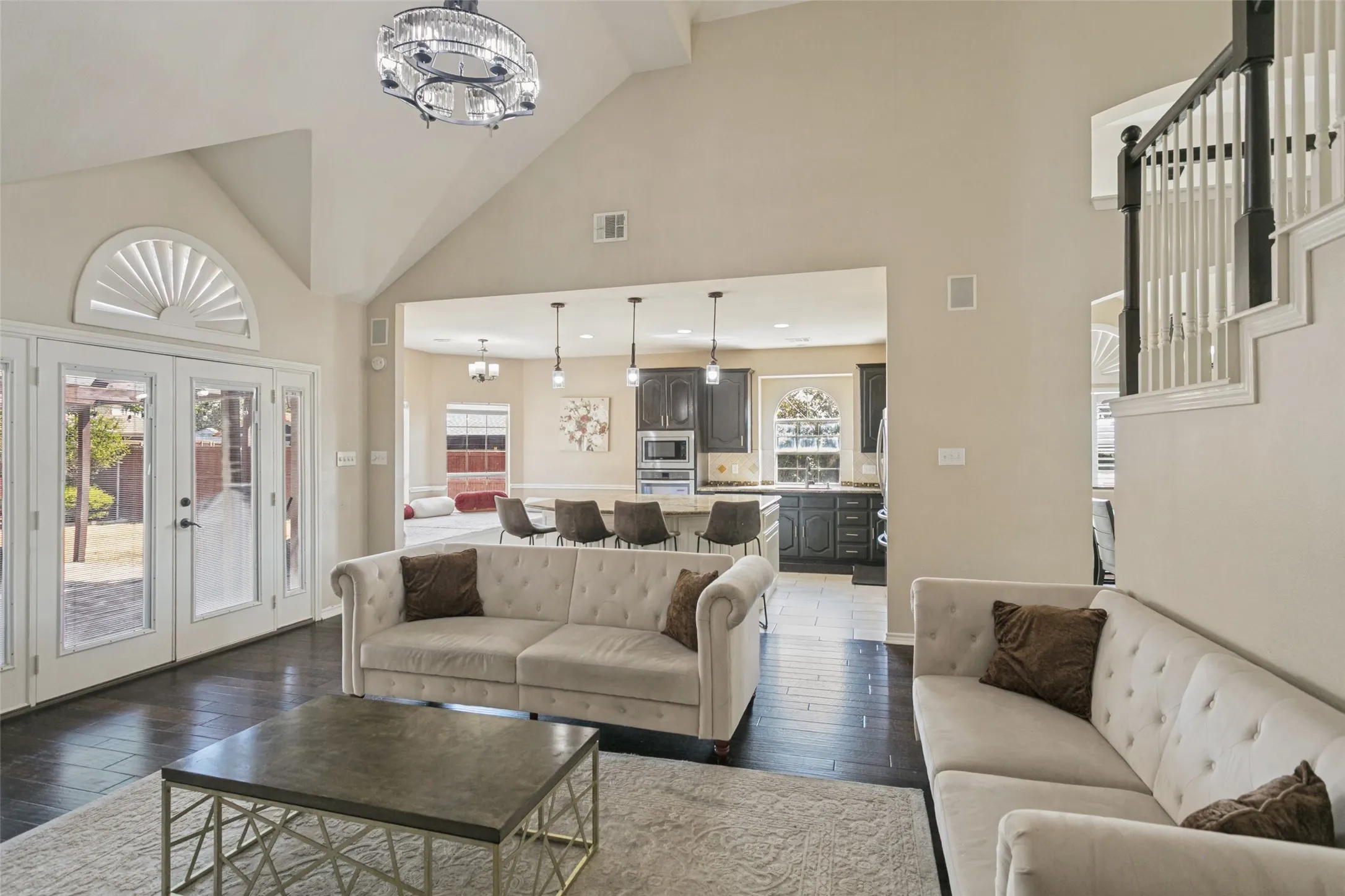 Vaulted ceilings with a decorative chandelier, dark wood-finish flooring, and French doors with an arched transom