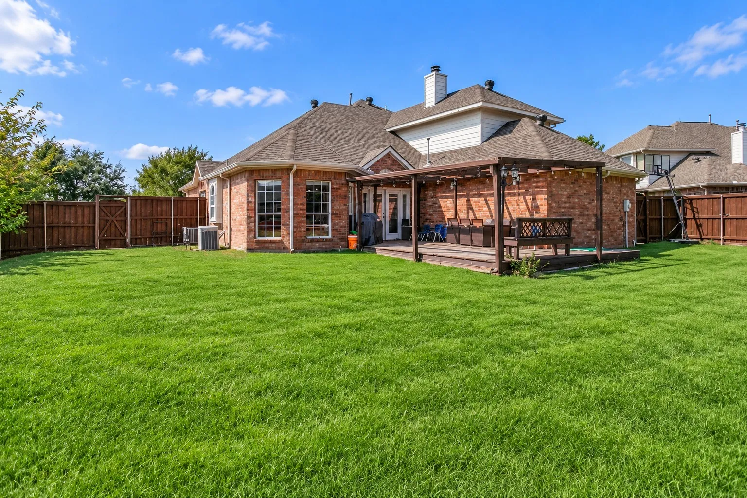 Expansive lawn with a wooden privacy fence, brick exterior, and a wood-decked patio featuring a pergola