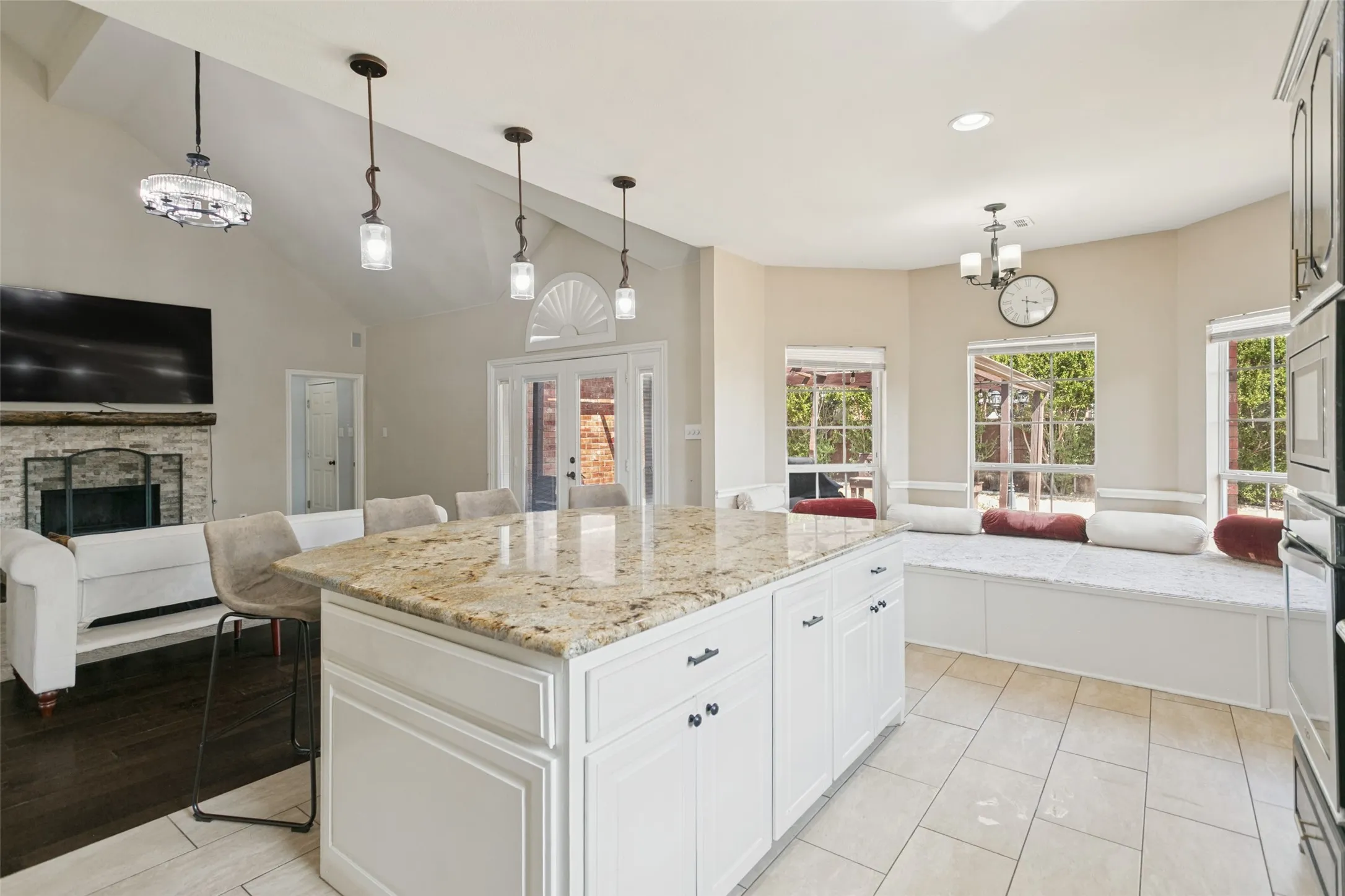 Spacious kitchen island with stone countertop, white cabinetry with dark hardware, built-in window seating, and vaulted ceiling