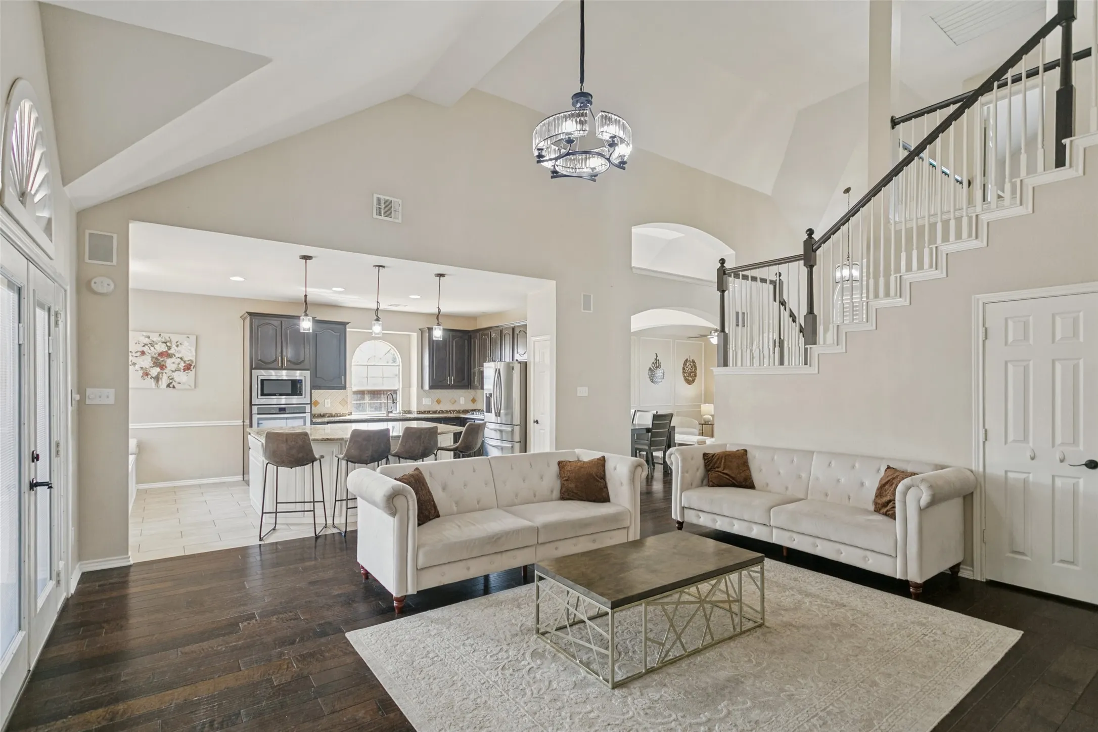 Vaulted ceiling with an architectural chandelier, dark wood-finish flooring, and a staircase featuring white balusters and dark wood handrails
